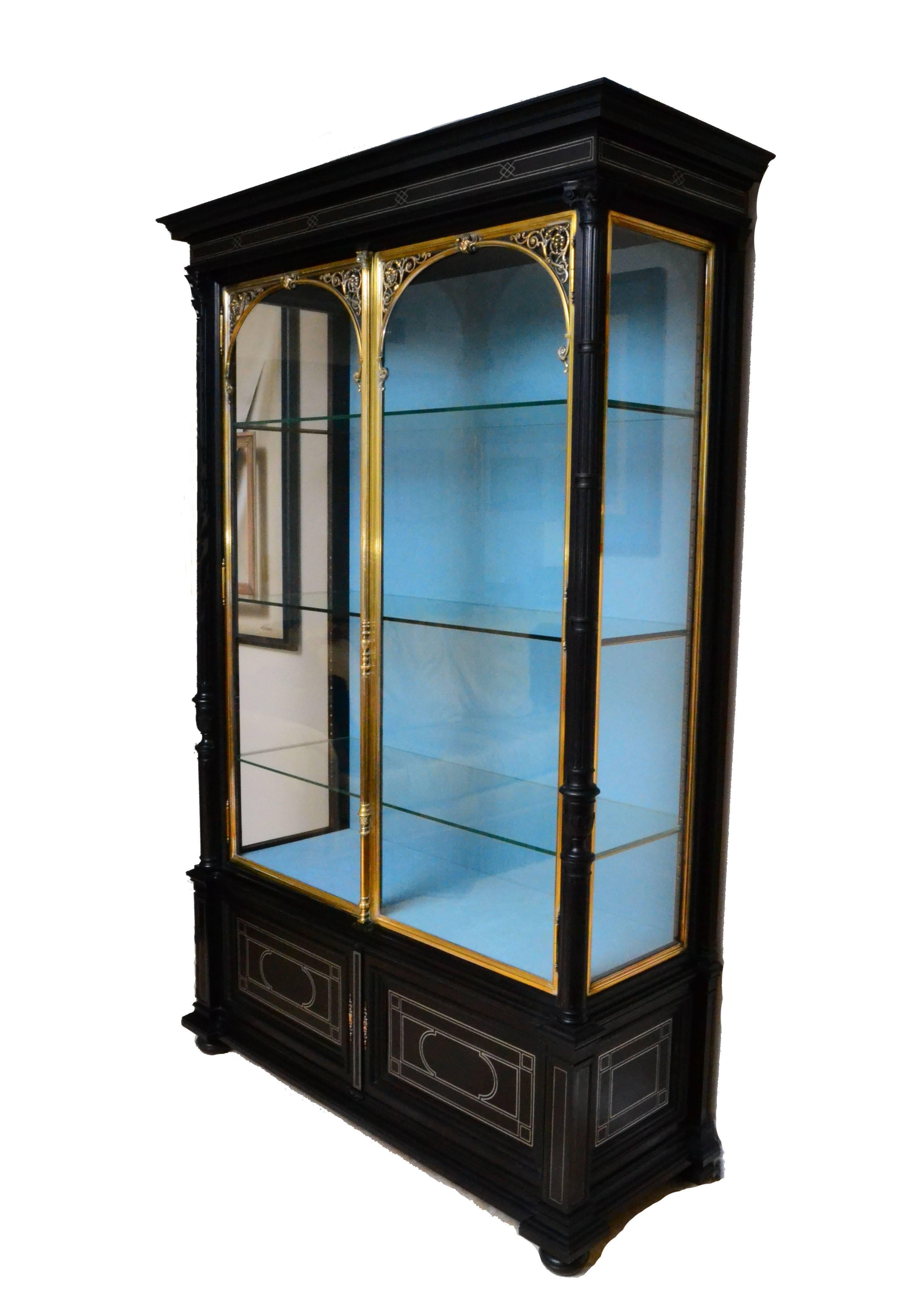 19th century ebonized vitrine. Side panelled glass set in brass frames. Fronted with a pair of glass doors also set in decorative brass frames. Key hole set in an elaborately turned escutcheon. Panelling on the front and side finished with brass