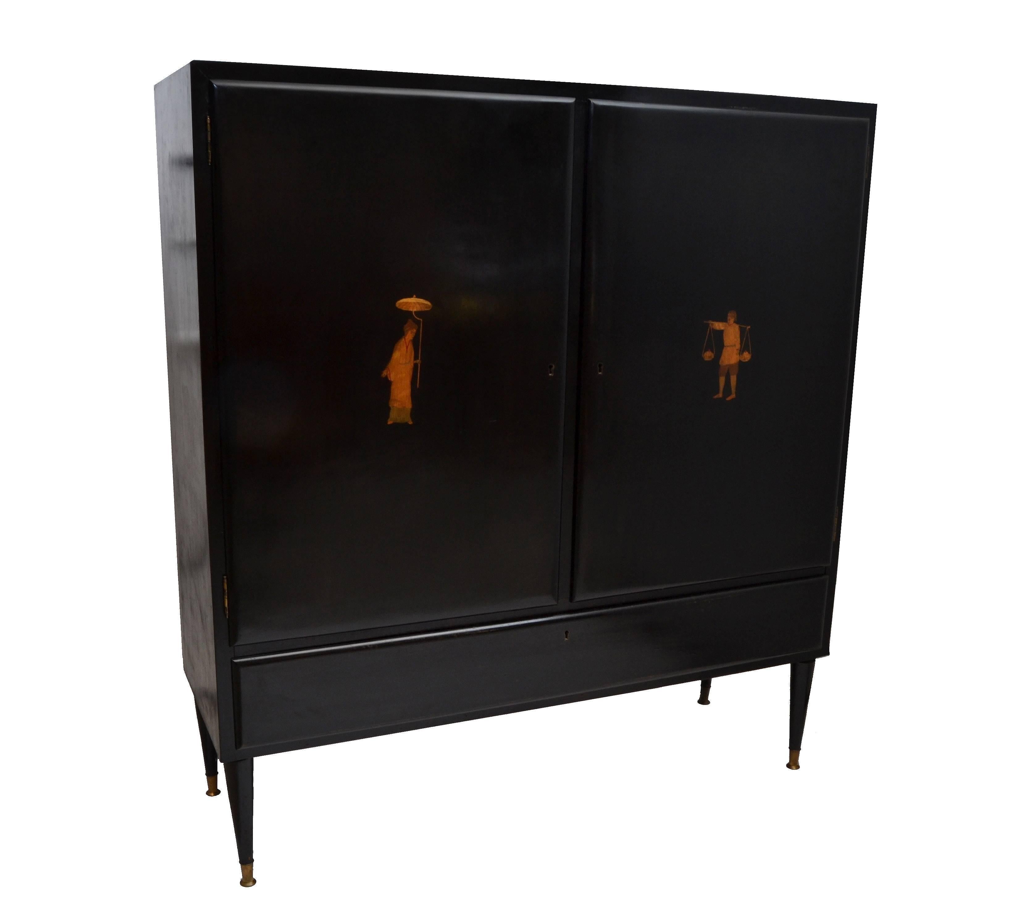 One of a kind wooden cabinet made in Milano, circa 1950 with brass detailed tapered legs.
Ebonized finish, two decorated doors displaying a man as well as a woman in marquetry, has a brass pull.
The interior features four glass shelves and the
