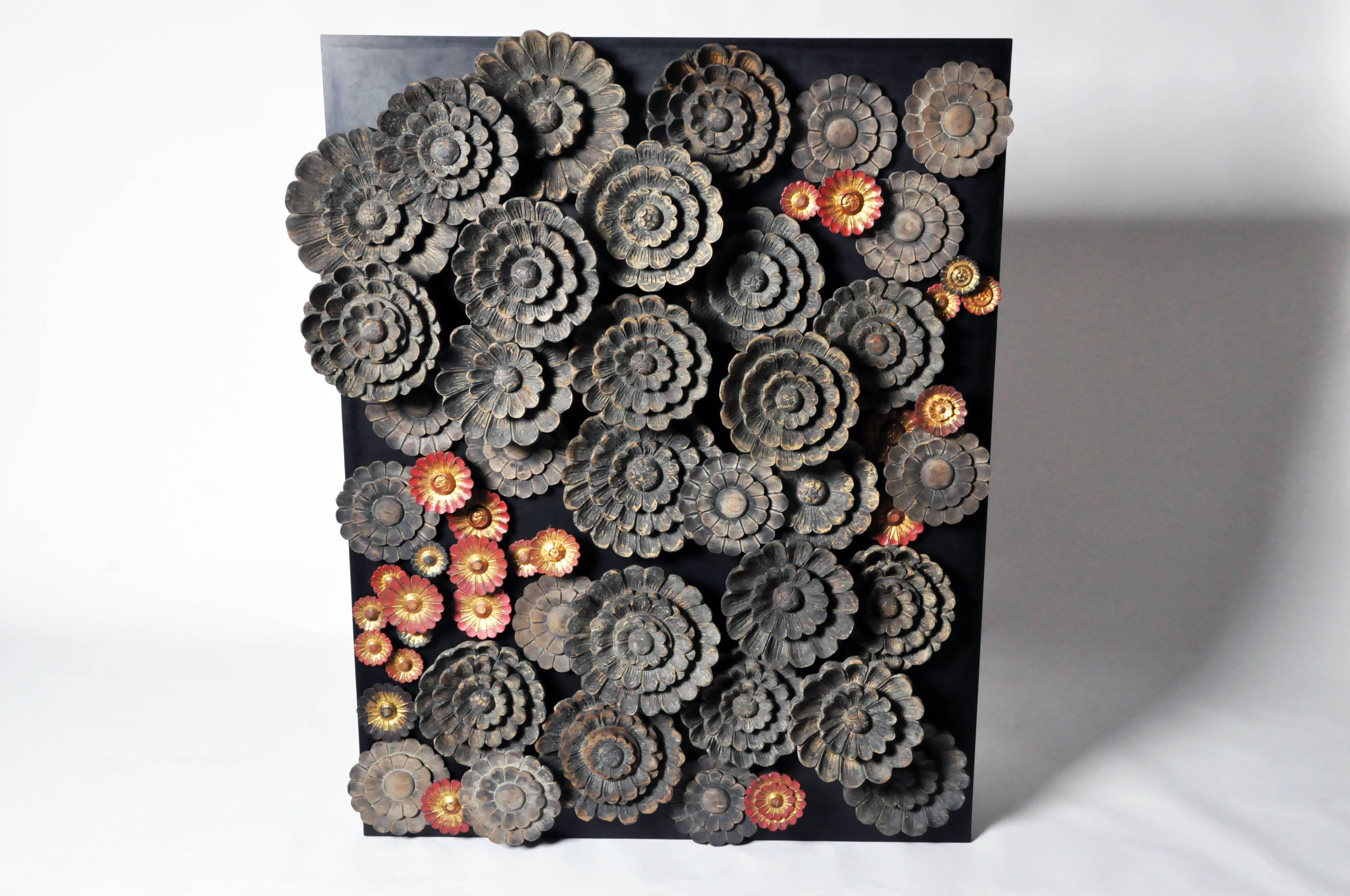 This three-dimensional wall sculpture features two types of hand-carved teakwood lotus blossoms; the larger having a matte black finish while the smaller have gold leaf centers surrounded by black or red lacquer. Mounted at various heights, the