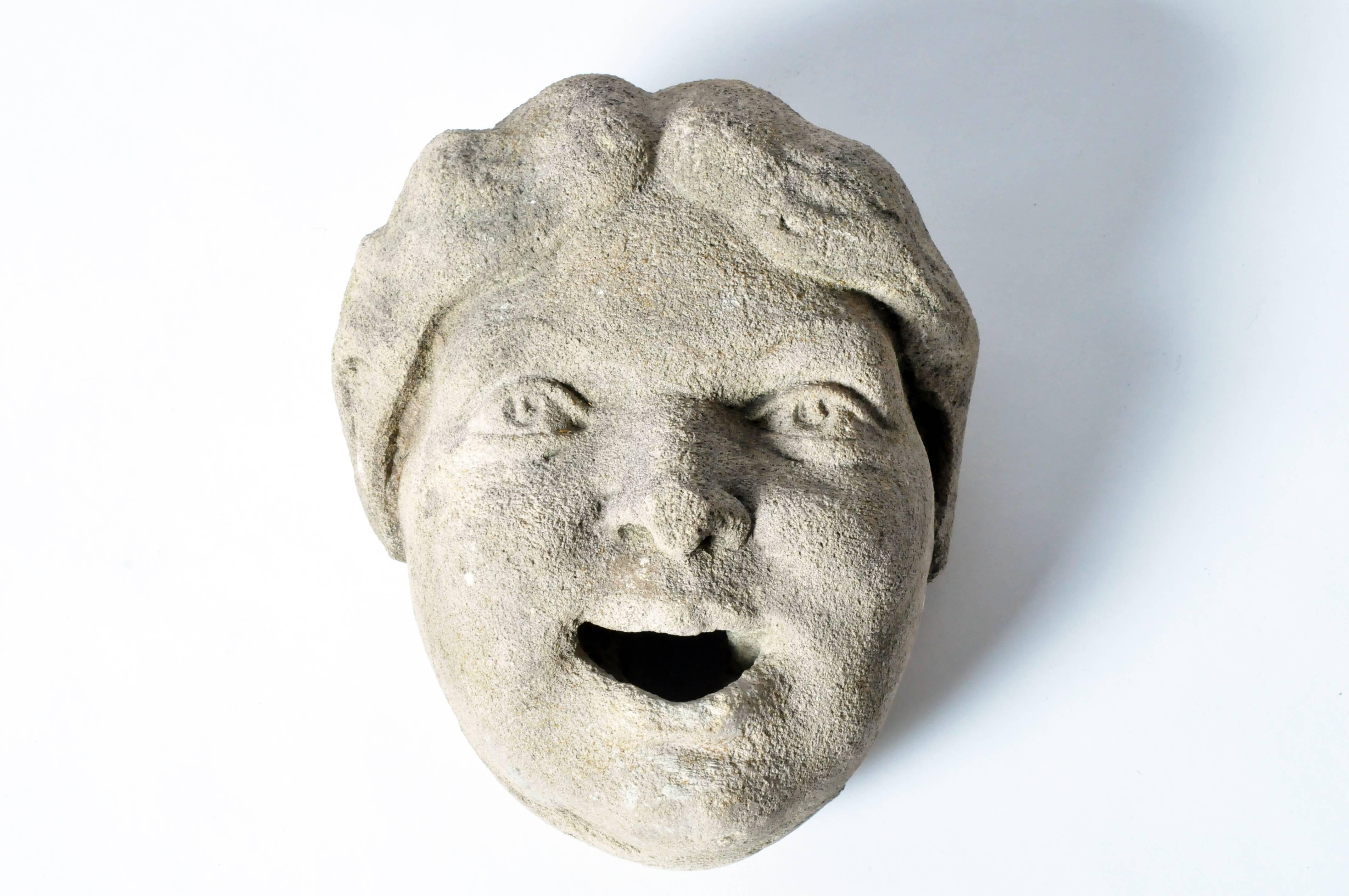 A remnant salvaged from a wall fountain, the face is likely that of a young boy. He is depicted laughing, mouth slightly open with full cheeks and a head of wavy hair.