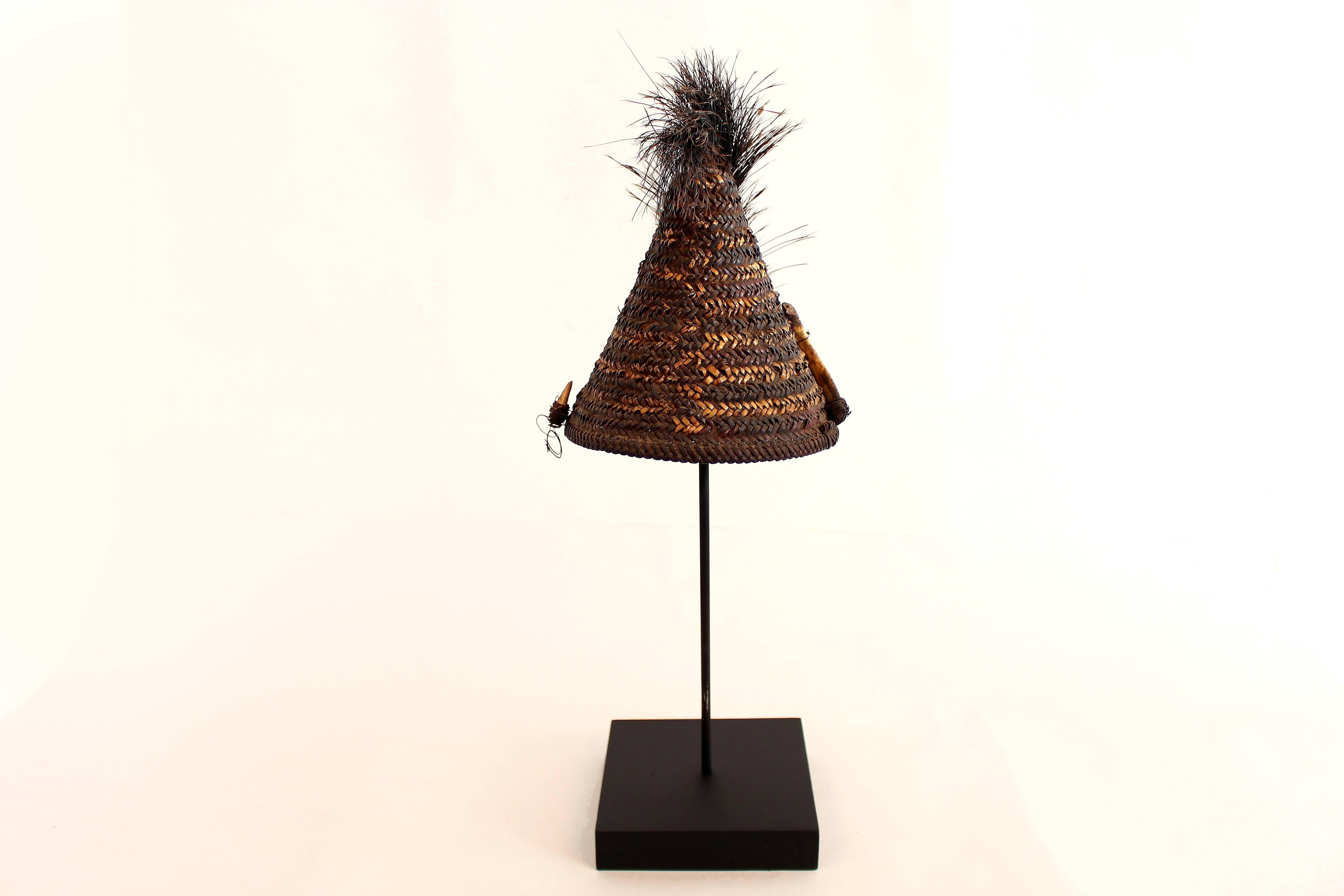 This woven hat features a plume of dark fur and a boar's tusk on one side. Though more decorative than protective, the accoutrements added symbolize social status. These particular items were trophies from a successful hunt.

Like the monumental