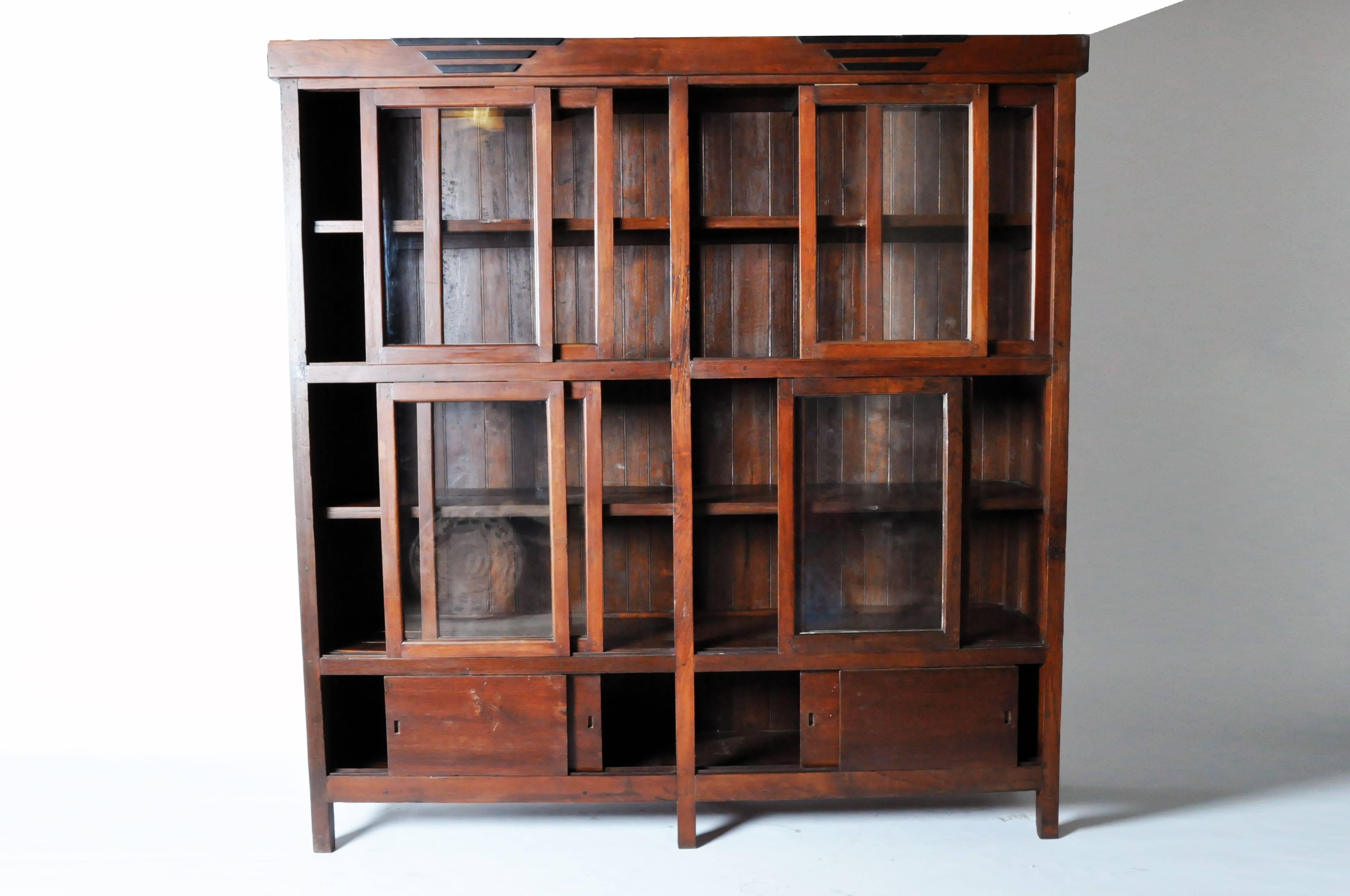 This Mid-Century Modern cabinet features an upper display case enclosed by four pairs of sliding doors with glass panes. At the base two pairs of sliding wood doors conceal additional storage space.