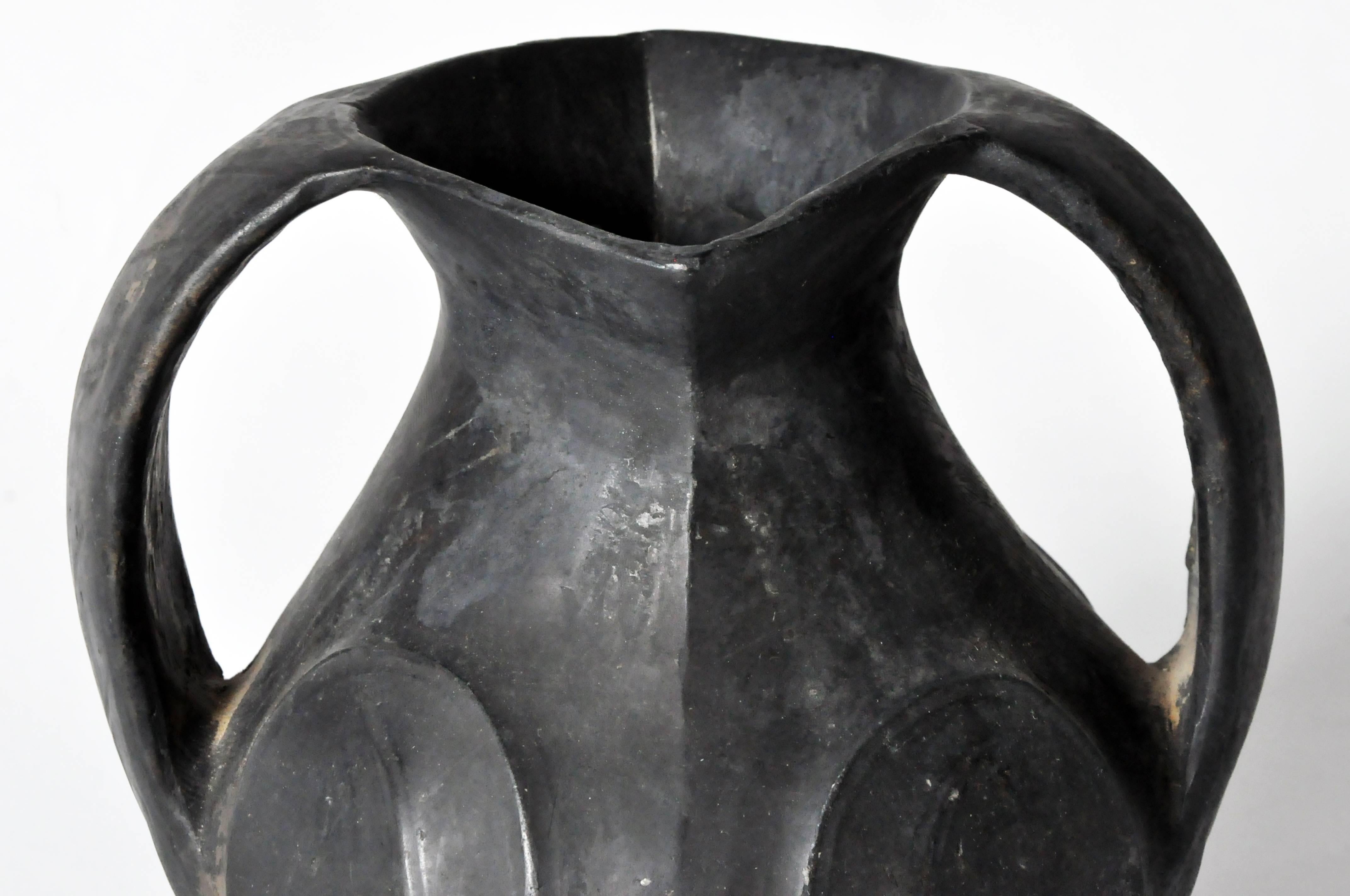 This Amphora-form vessel has a diamond shaped lip to which a pair of ribbon-like handles is attached. Extending down past the tapered neck, they connect with the bulbous body that features a swirl decoration under the matte black glaze.