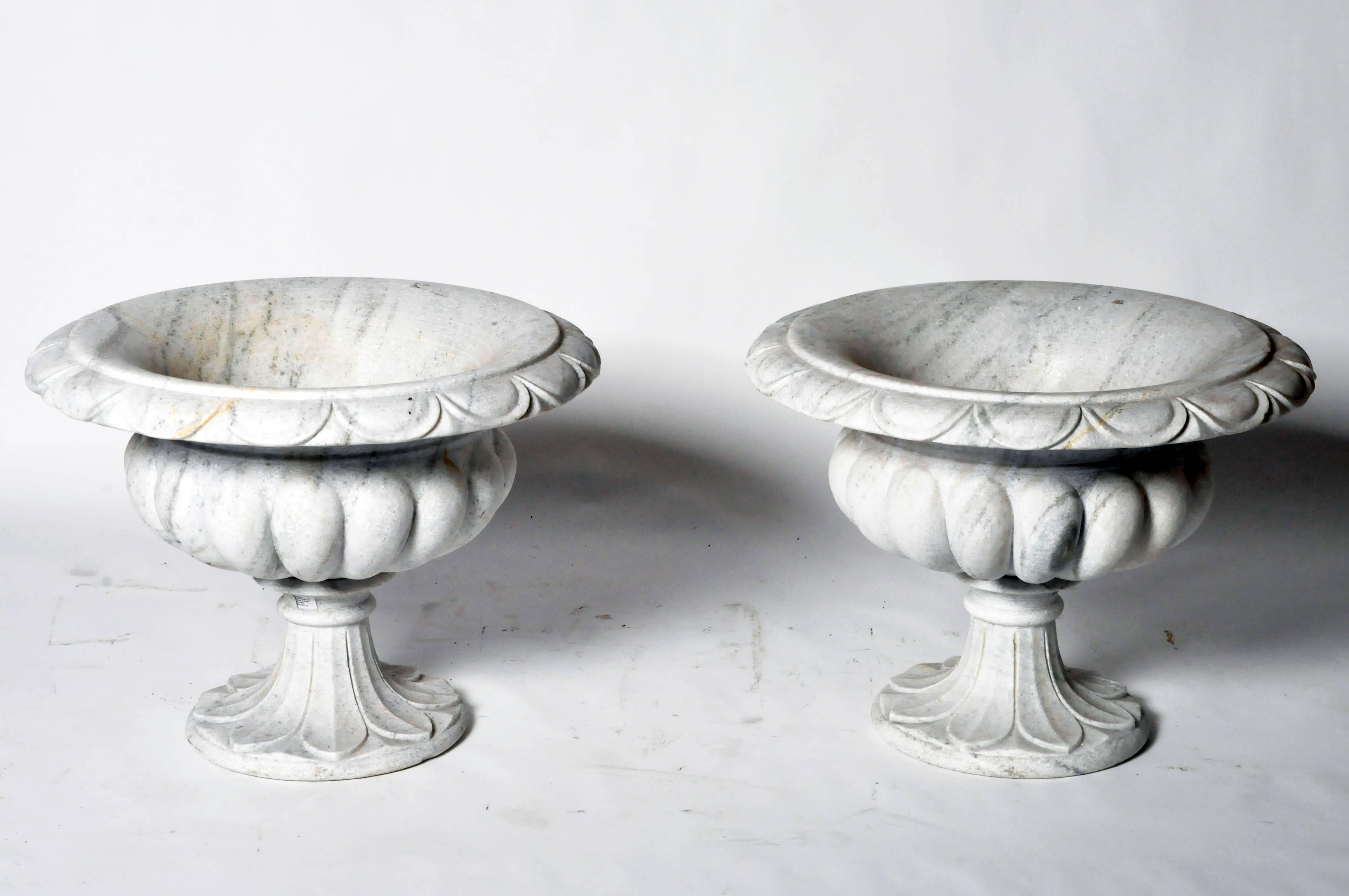 The variegated marble perfectly compliments this shapely urn. It is beautifully carved from the swag-like patterned rim, down through the ribbed body supported by a short, foliate patterned pedestal base. The pair would look exceptional inside or