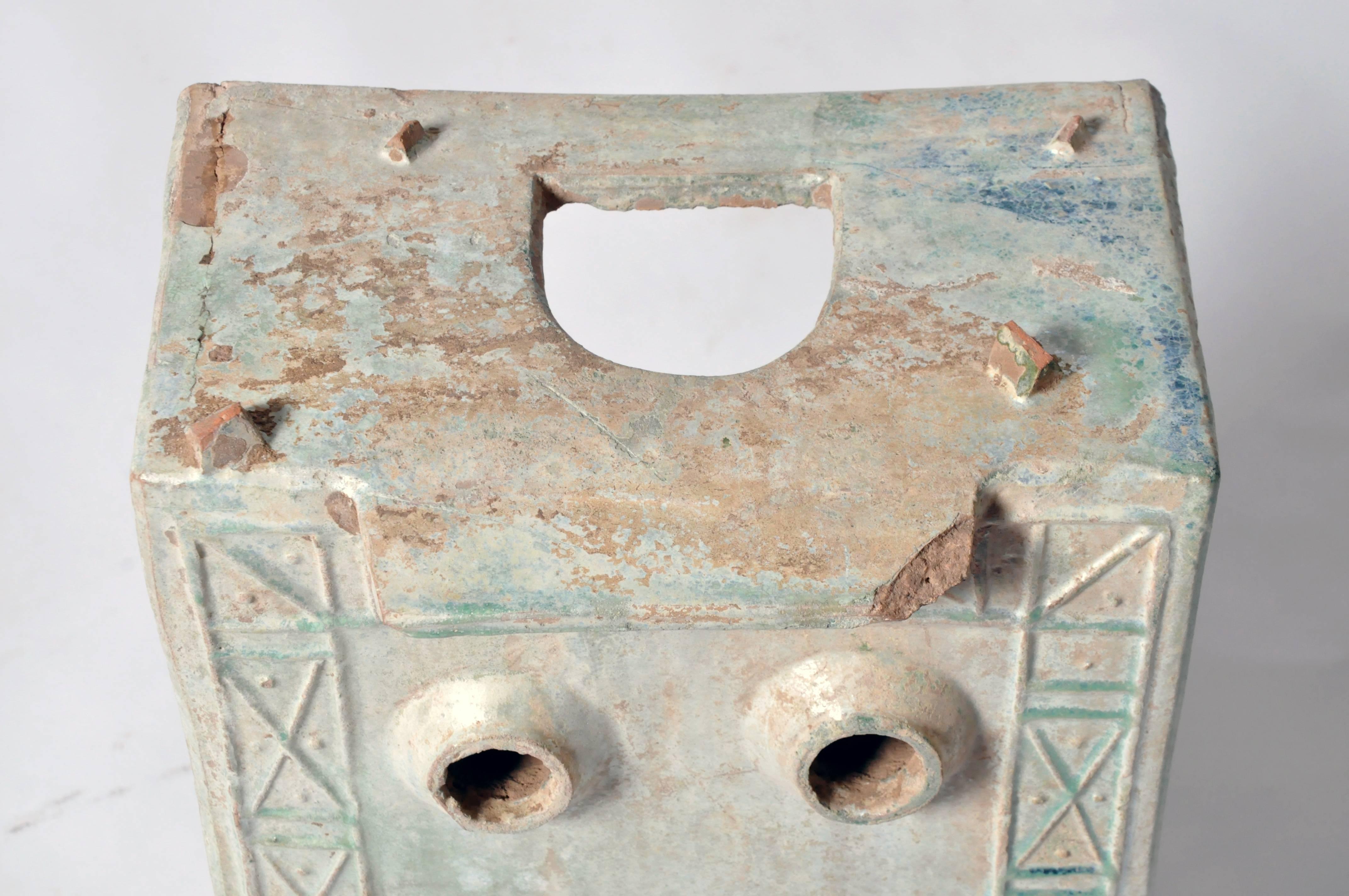 This squat, rectangular piece of tomb pottery features an arched door below a trapezoidal pediment, three circular openings on its top and an incised, decorative border in a geometric pattern. Its light green glaze has developed a handsome