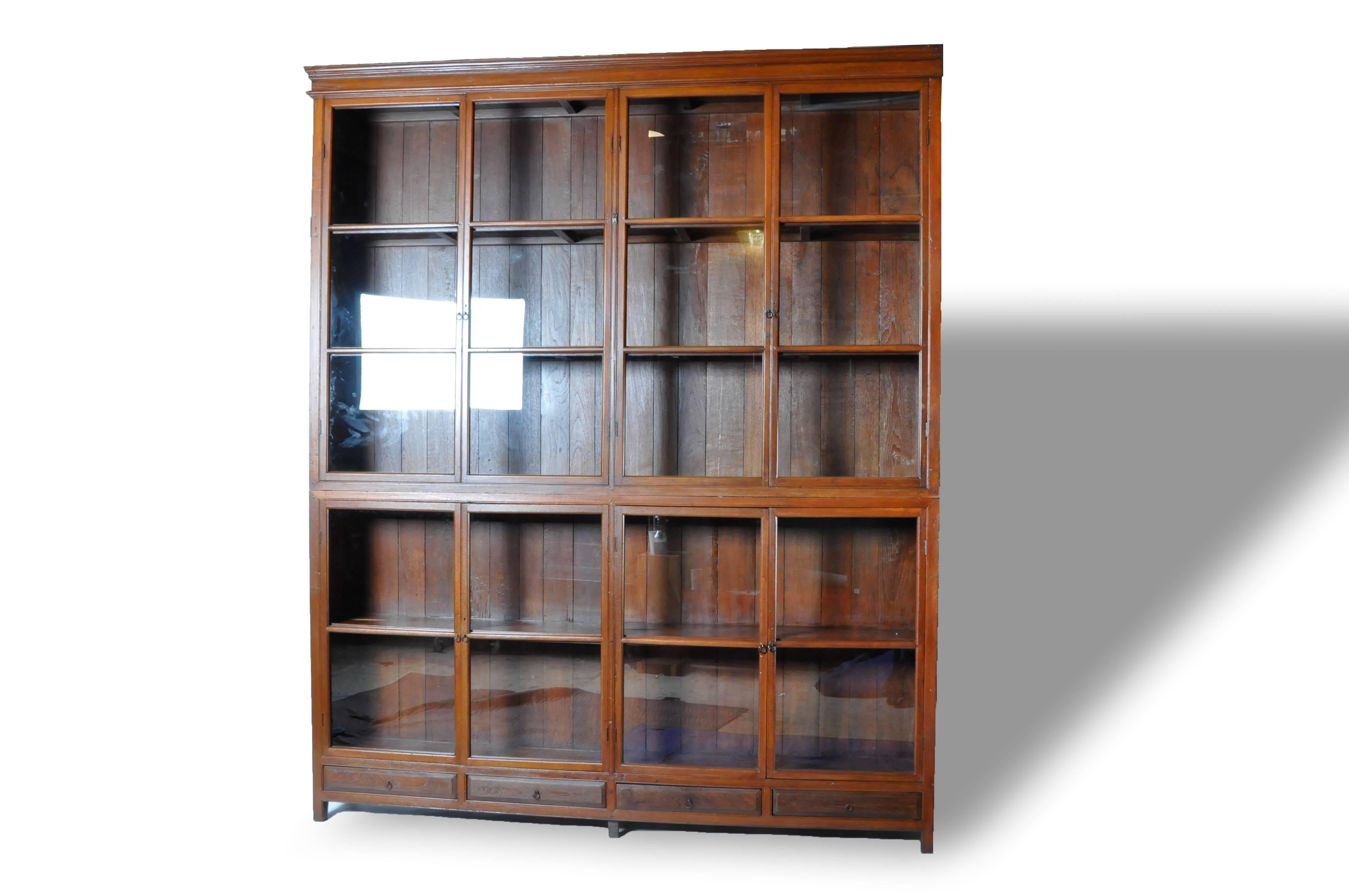 This impressive British Colonial bookcase comes in two parts; both the top and bottom have two pairs of glass paned doors that open to compartments lined with shelves. The lower section boasts ample storage space in the form of four drawer.