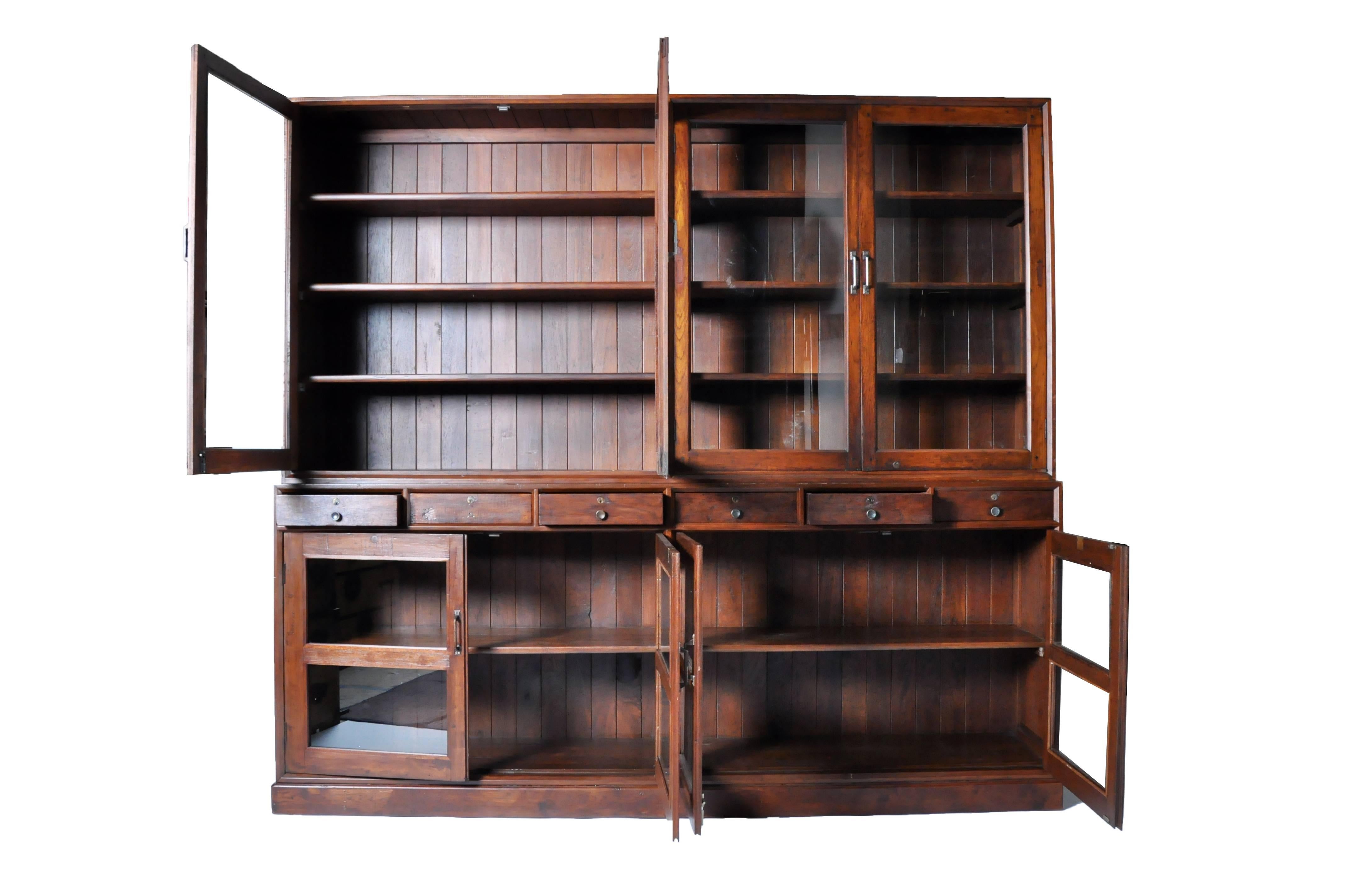 This impressive British Colonial cabinet comes in two parts; both the top and bottom display case features two pairs of glass paned doors that open to compartments lined with shelves. The top section boasts ample storage space in the form of two