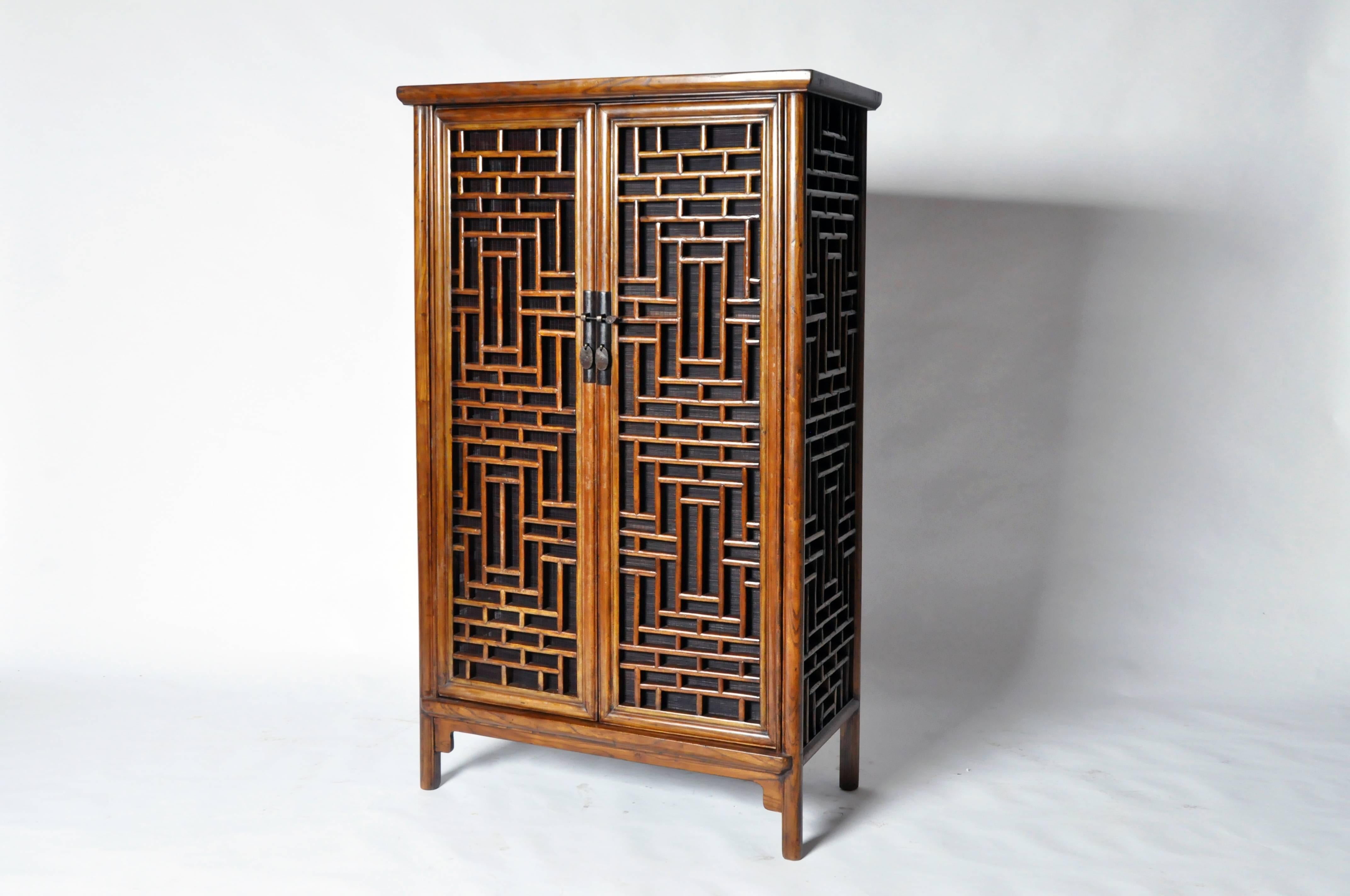 This elegant Chinese lattice cabinet is made from elmwood with restorations. It features shelving inside for ample storage.