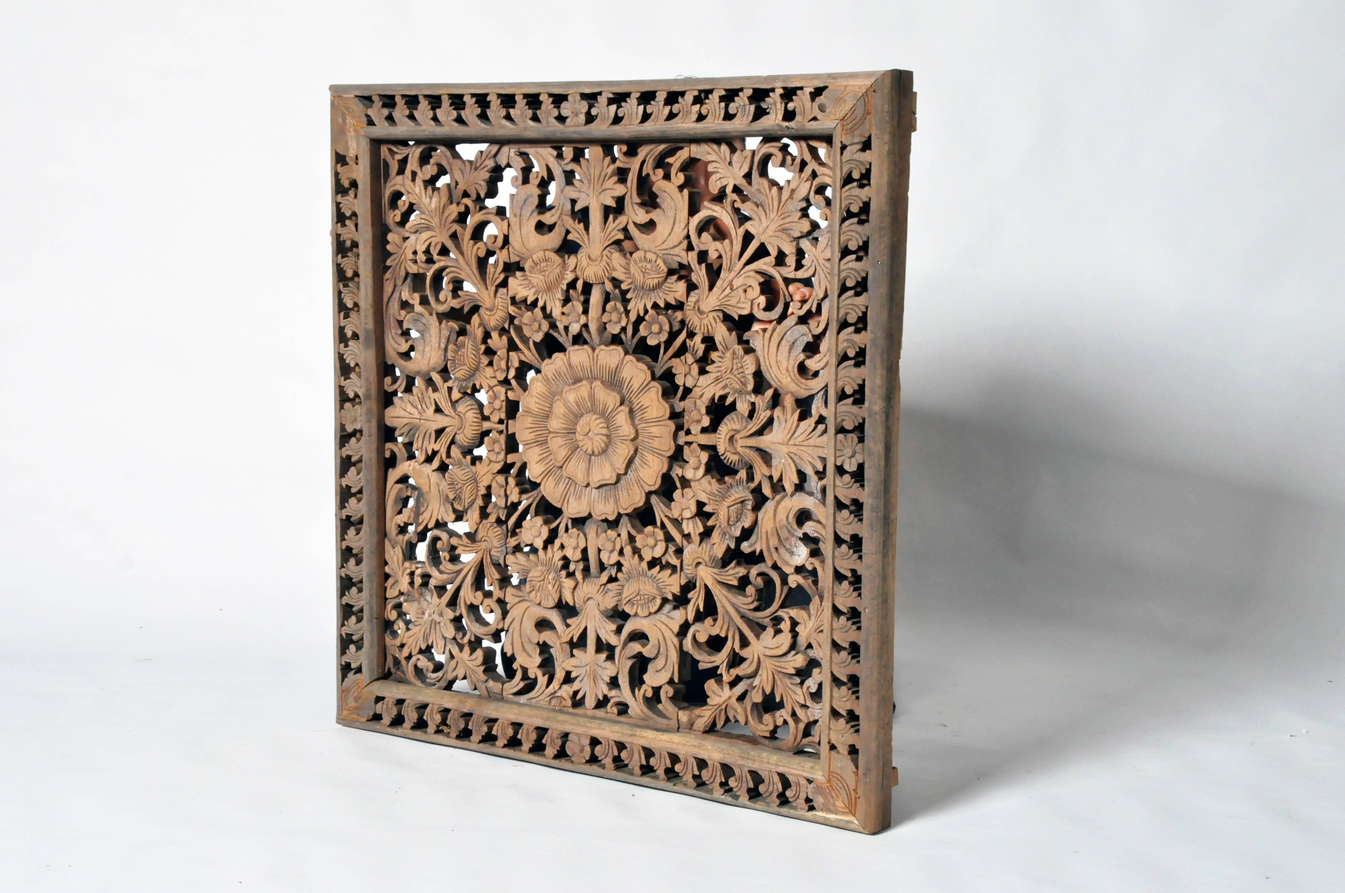 This intricately hand-carved, the panel depicts a central medallion of blossoms and C-scroll leaf decorations that are framed by a repetitive stylized border. It is made from teakwood and is from the northern part of Thailand.