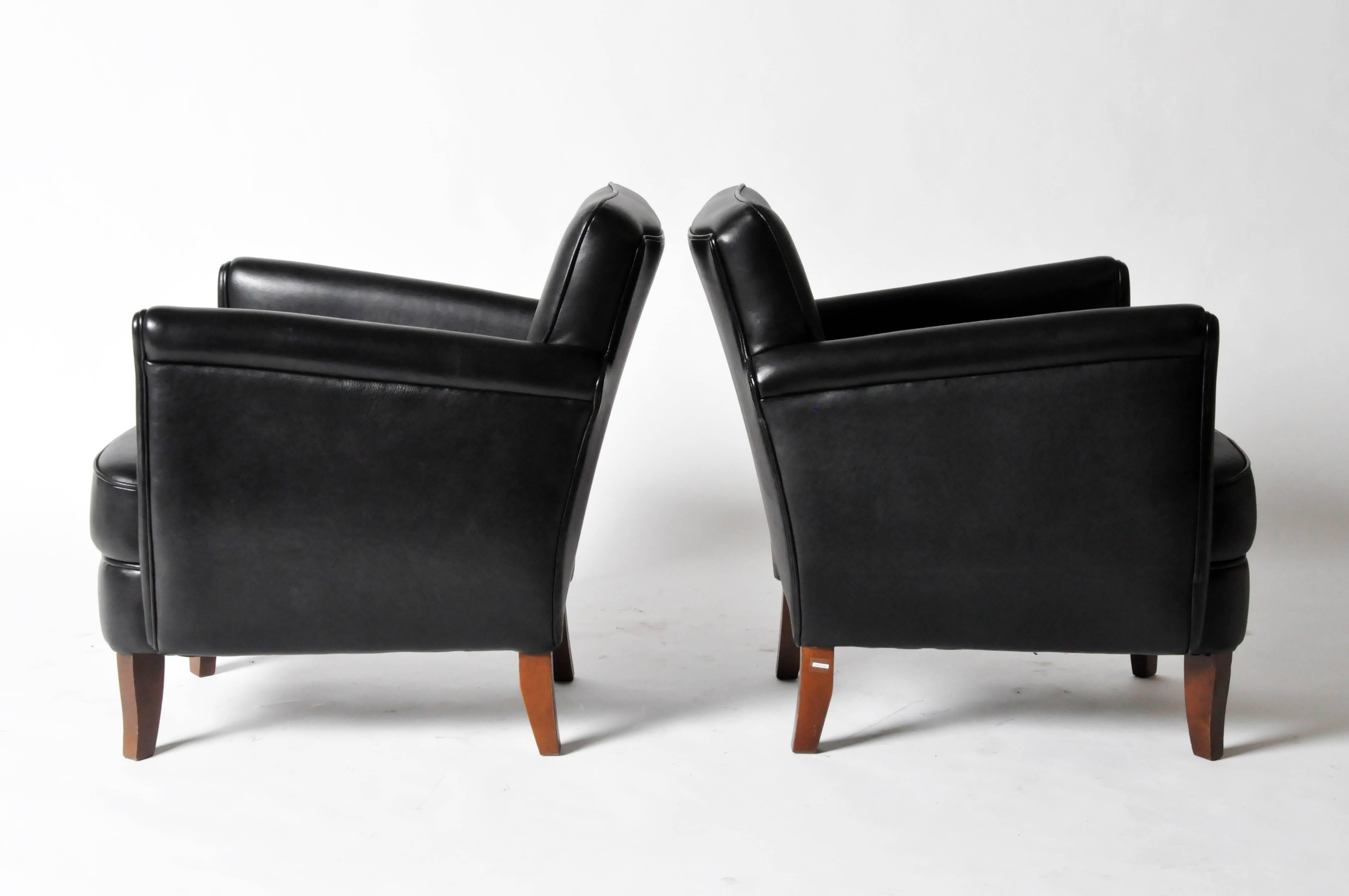 These compact chairs are upholstered in black leather and raised on square wooden legs.