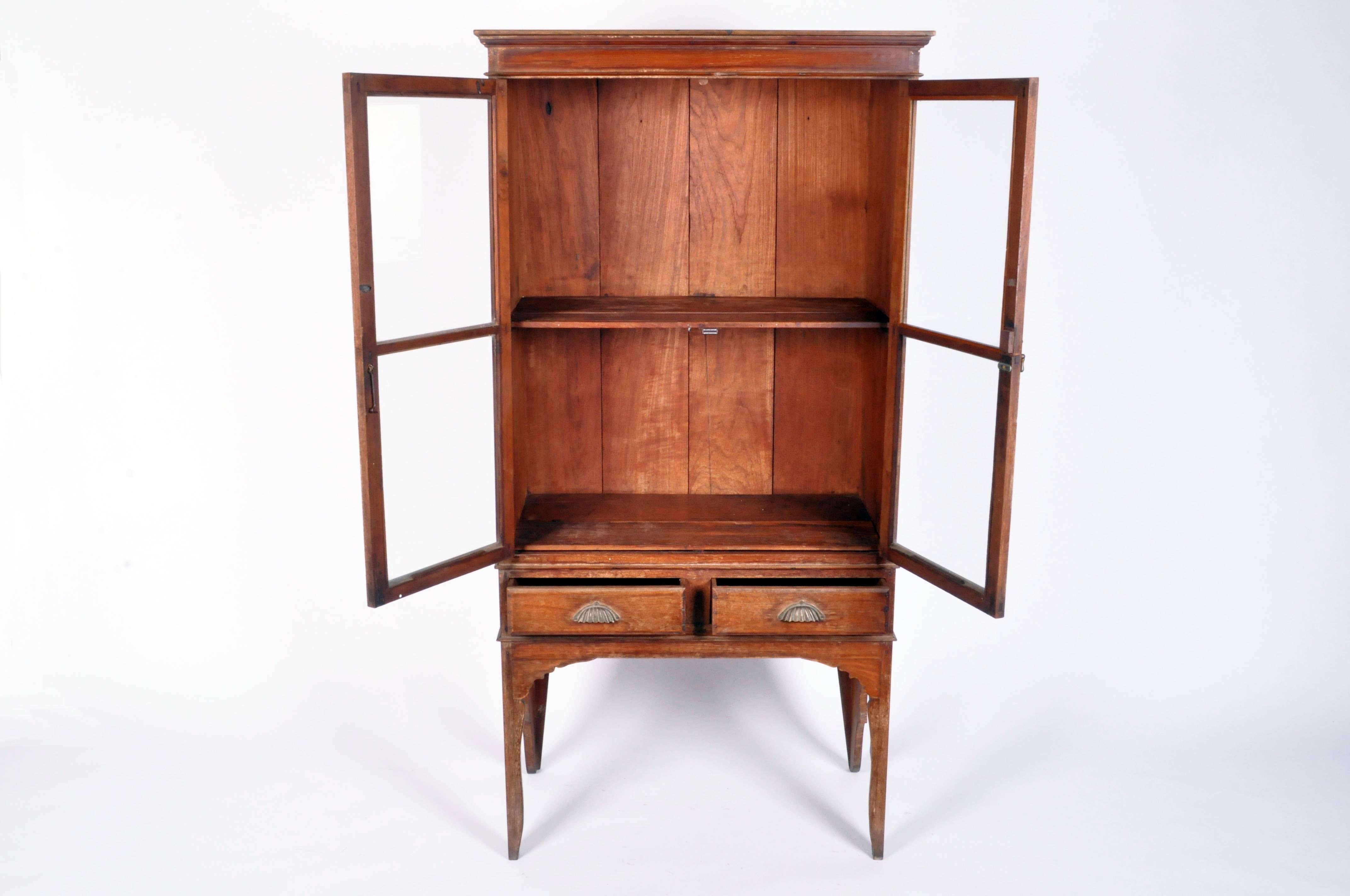 This Northern Thai display cabinet came from Chiang Mai and is made from solid teak wood. Inside it features a shelf and below are two drawers for storage. The style of the piece is very angular and simple. Northern Thai pieces are a mix of Thai