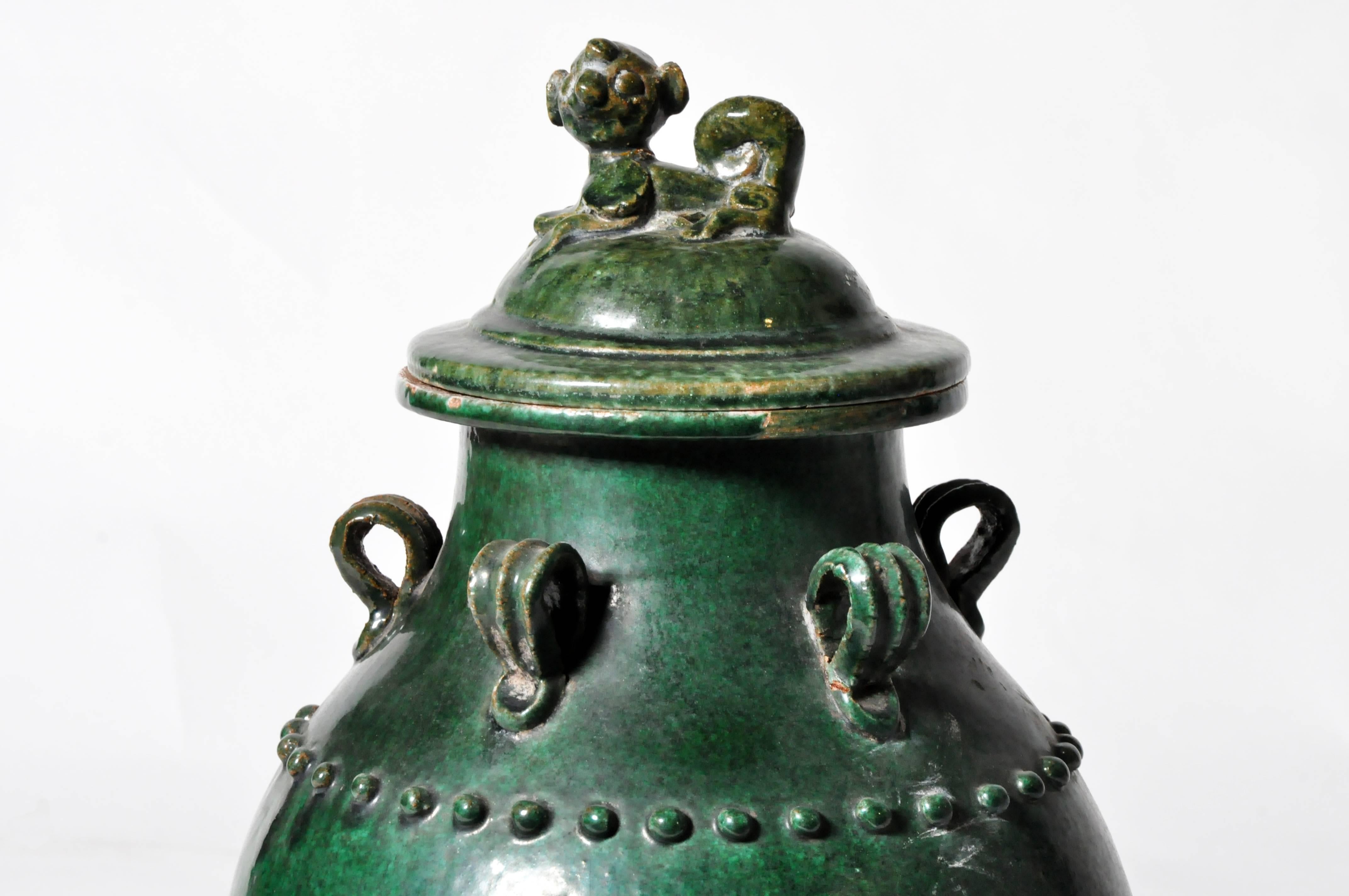 This earthenware pot has five handle rings, a lid topped with a miniature 'Fu' Dog, and a glistening patina. Its rich green hue comes from a traditional glaze of lead and copper, used in display pieces and funerary offerings since the late Han