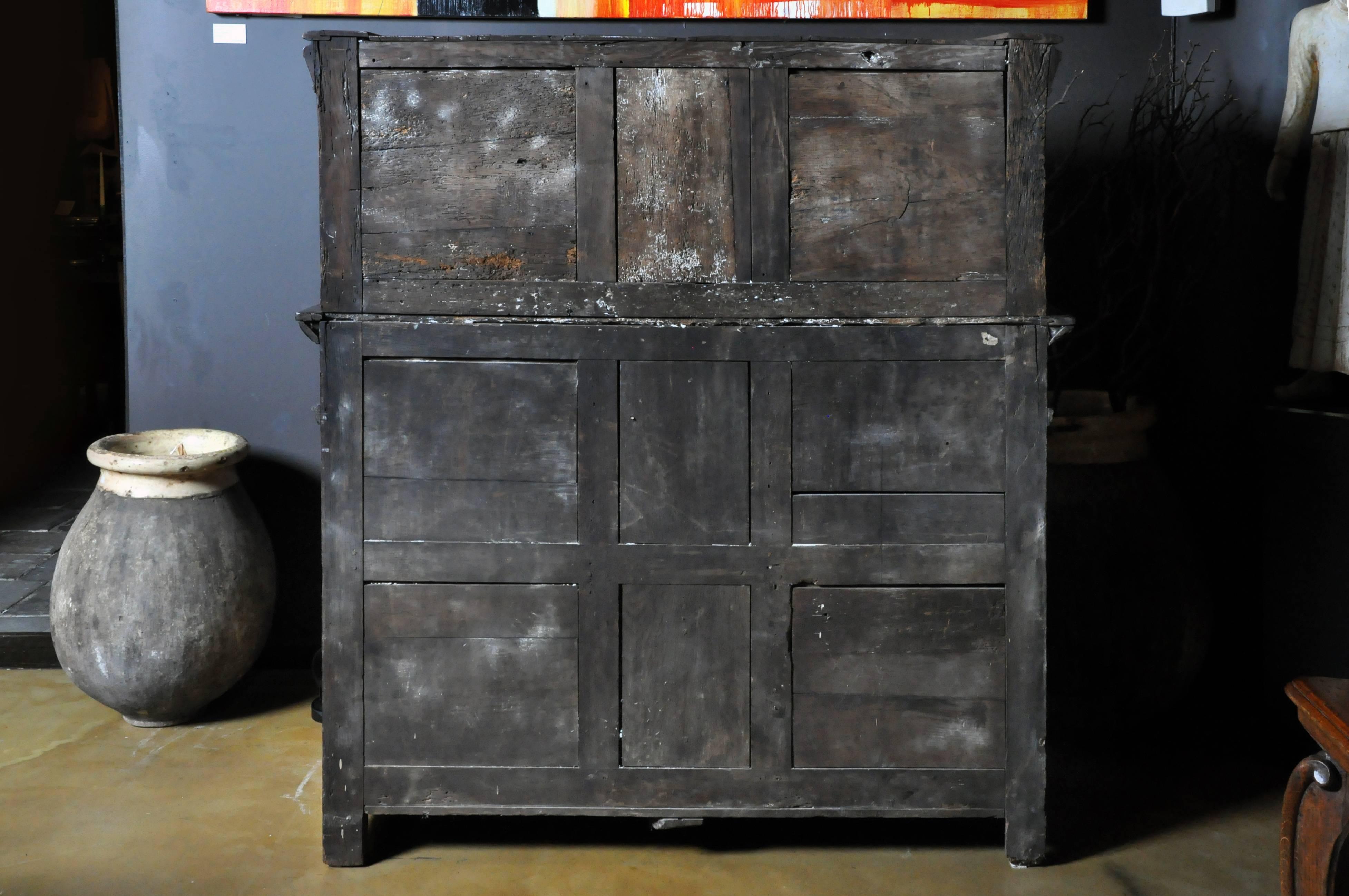 Hand-carved oakwood, 18th century, possibly earlier. Original finish throughout and no replacement or missing parts. Hardware is hand-forged iron. Marquetry decoration on door panels and crown. False drawers flank operable center drawer. All drawer