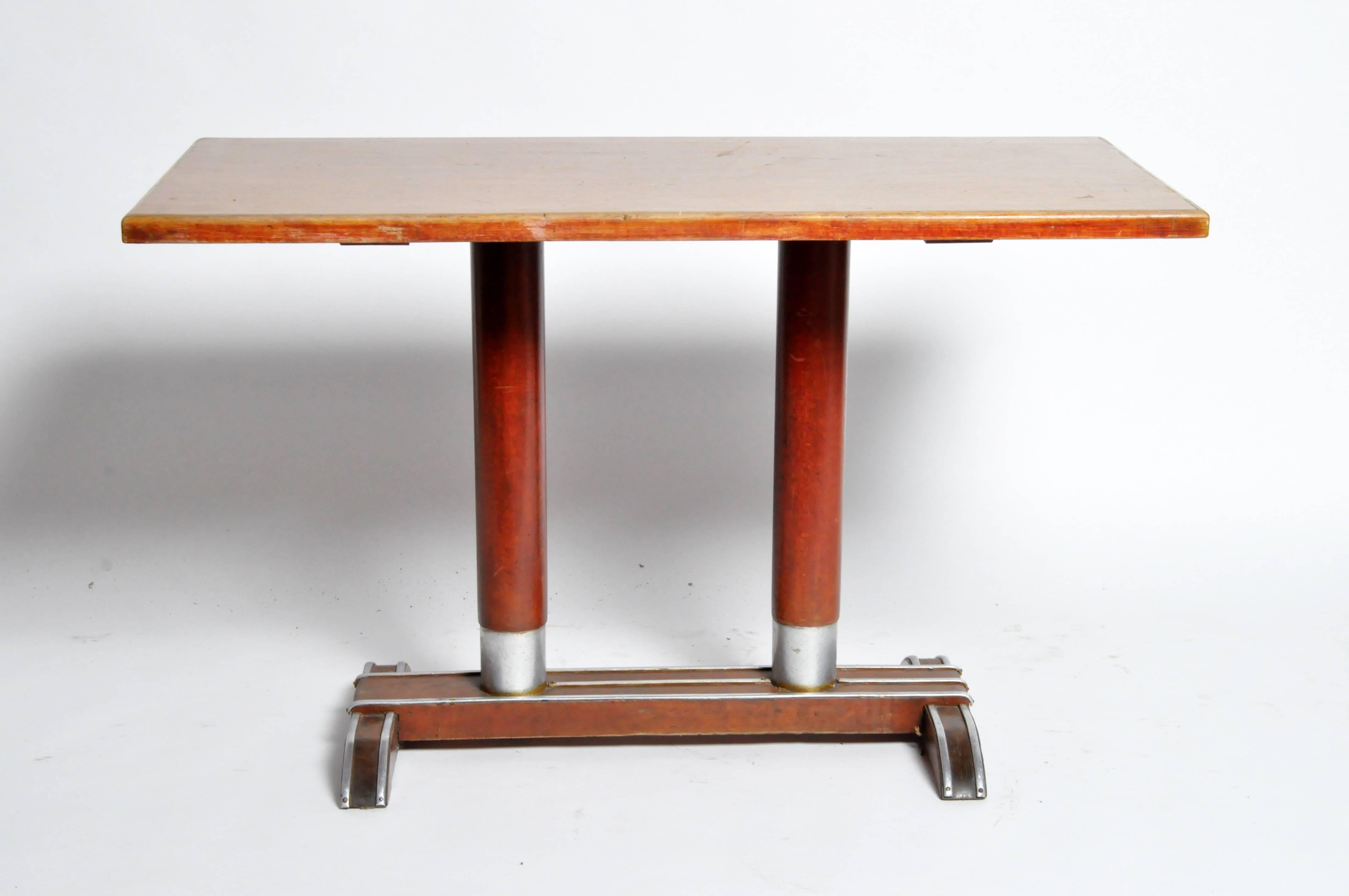 This Mid-Century Modern piece has a touch of Art Deco flare as seen in the “Streamline Moderne” metal trim decoration along the base. The rectangular top provides a sizeable work surface for use as a worktable or desk, and comfortably seats four if