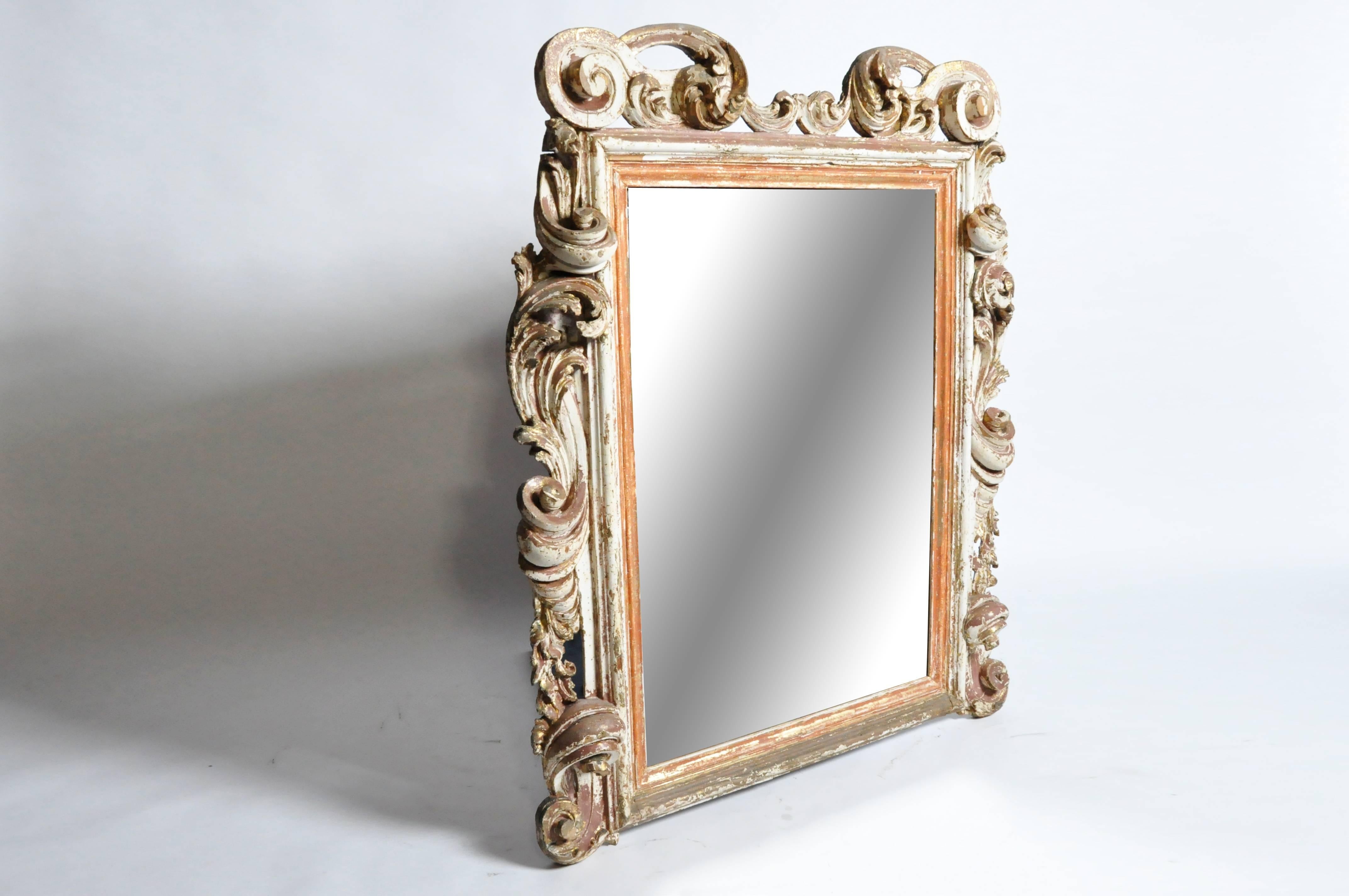 This elegant early 19th Century mirror is from Italy and was made from pine wood, gold leaf, and red and white pigments, c. 1800. This mirror features beautiful carved scroll-work around the mirror.
