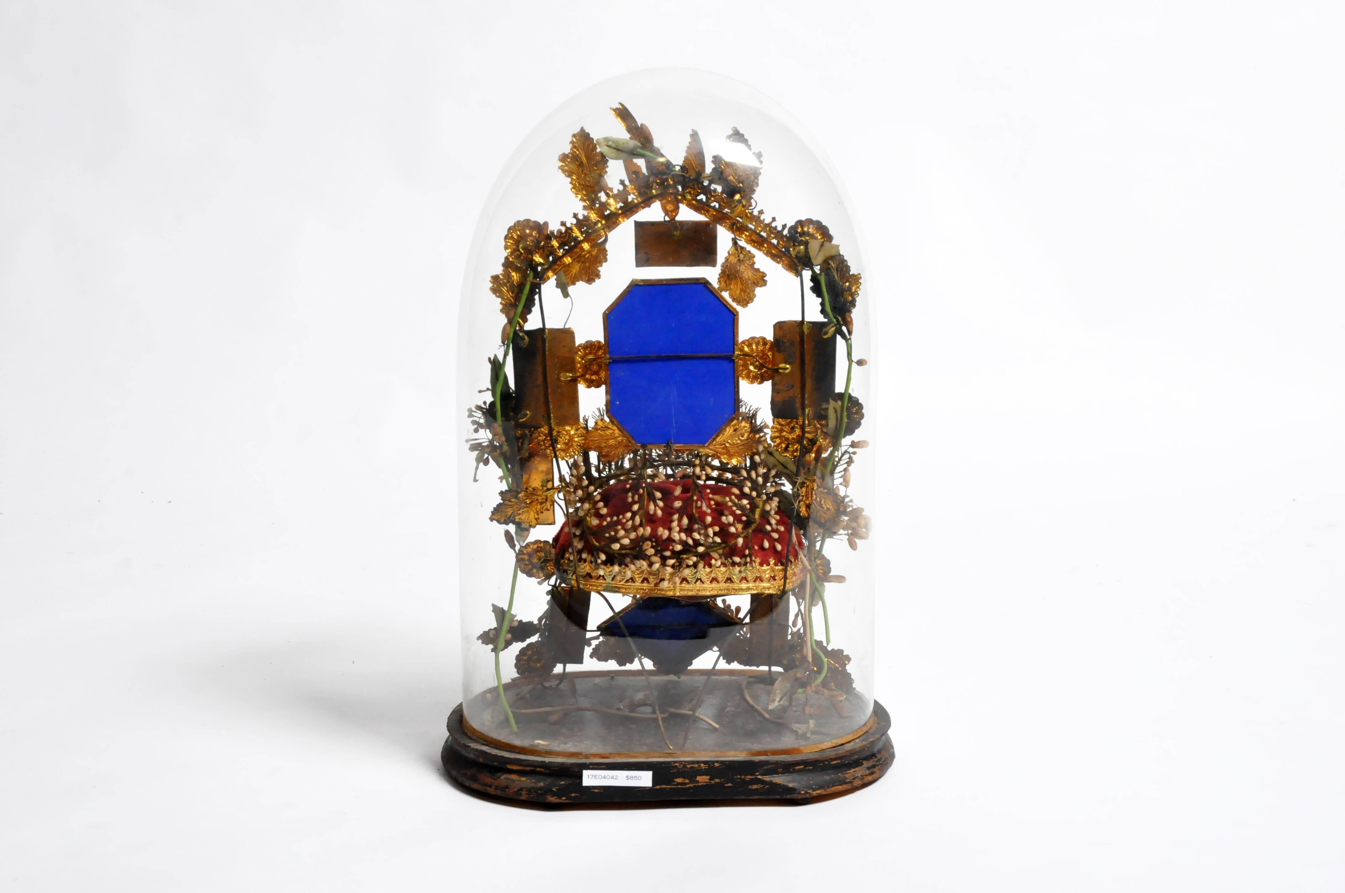 Quite the curiosity, this glass dome is more like a time capsule. Inside a miniature wire chair—with upholstered cushion—has a frame and legs made of gilt foliage, porcelain flowers, and mirrored glass. A bird-form finial holding a wreath of laurel