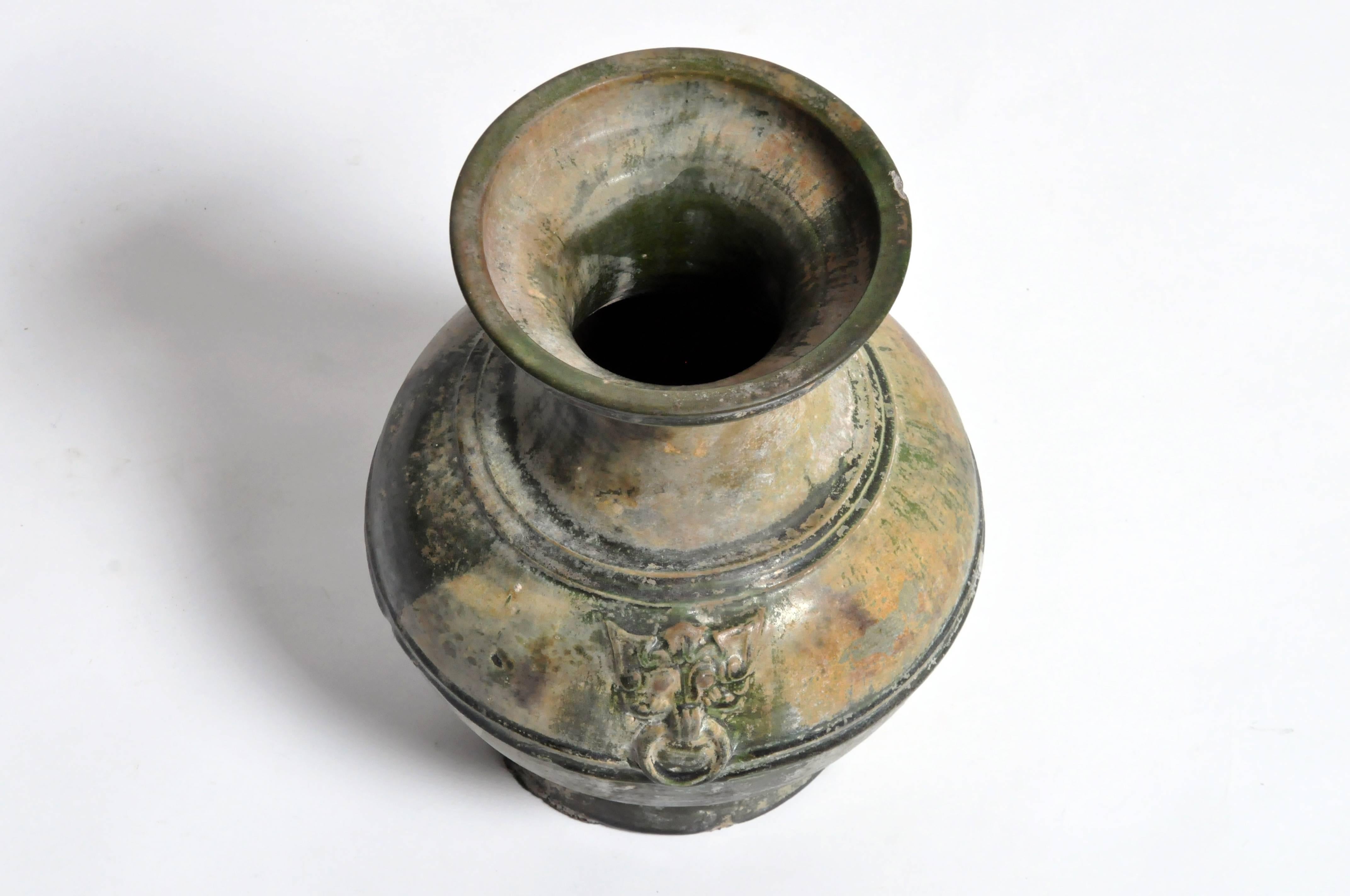 This “Hu” Vessel is from the Han Dynasty (220 - 280 AD) and was made from green glazed ceramic in the form of a bronze vessel. Molded rings indicate bronze vase model. This piece features much iridescence and calcification due to long burial in tomb.