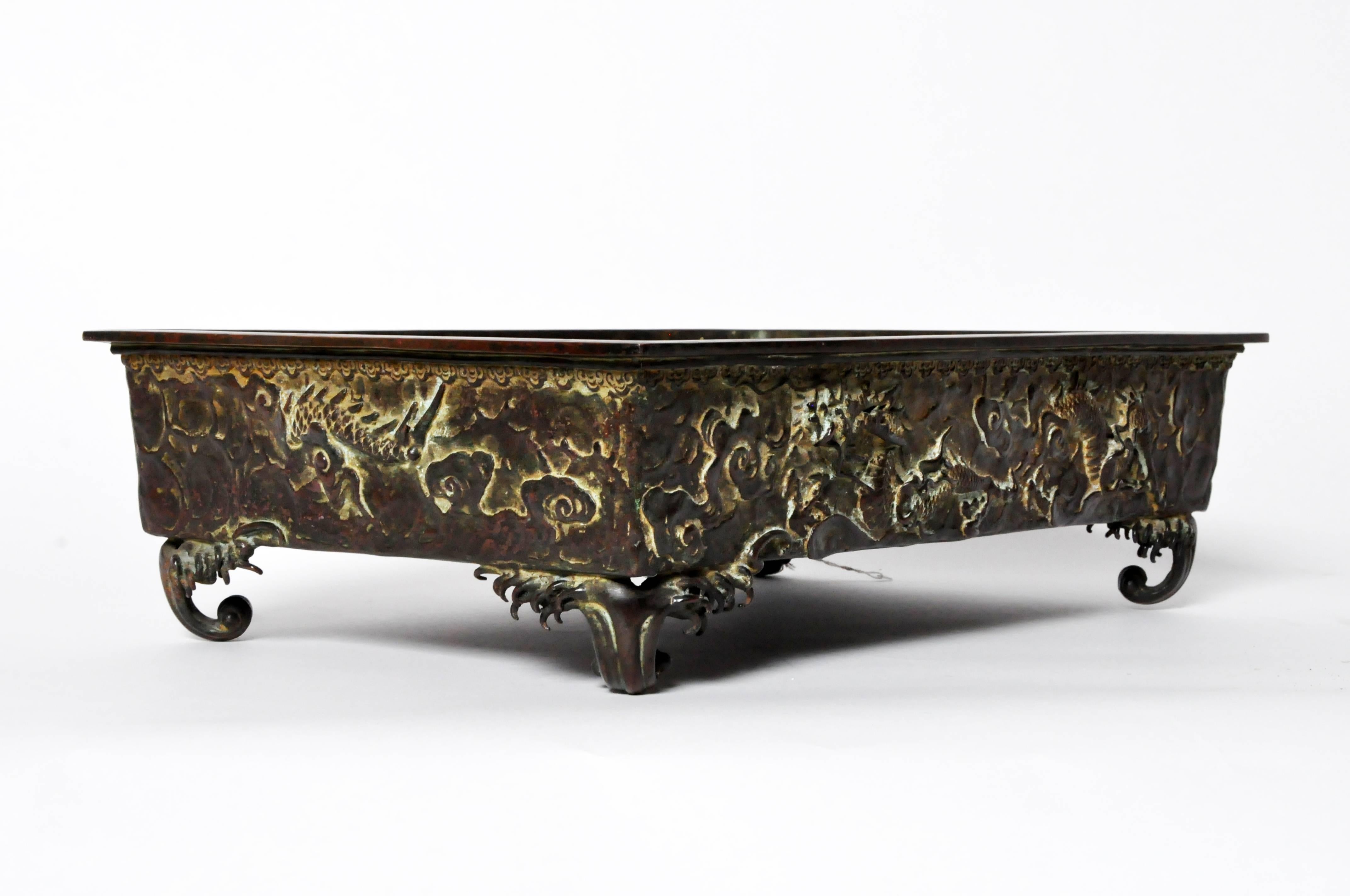 This antique 19th century Japanese bronze rectangular censer decorated with moulded dragons against a patterned cloud form background, standing on four scroll feet. The censer measures approximately 17 3/4