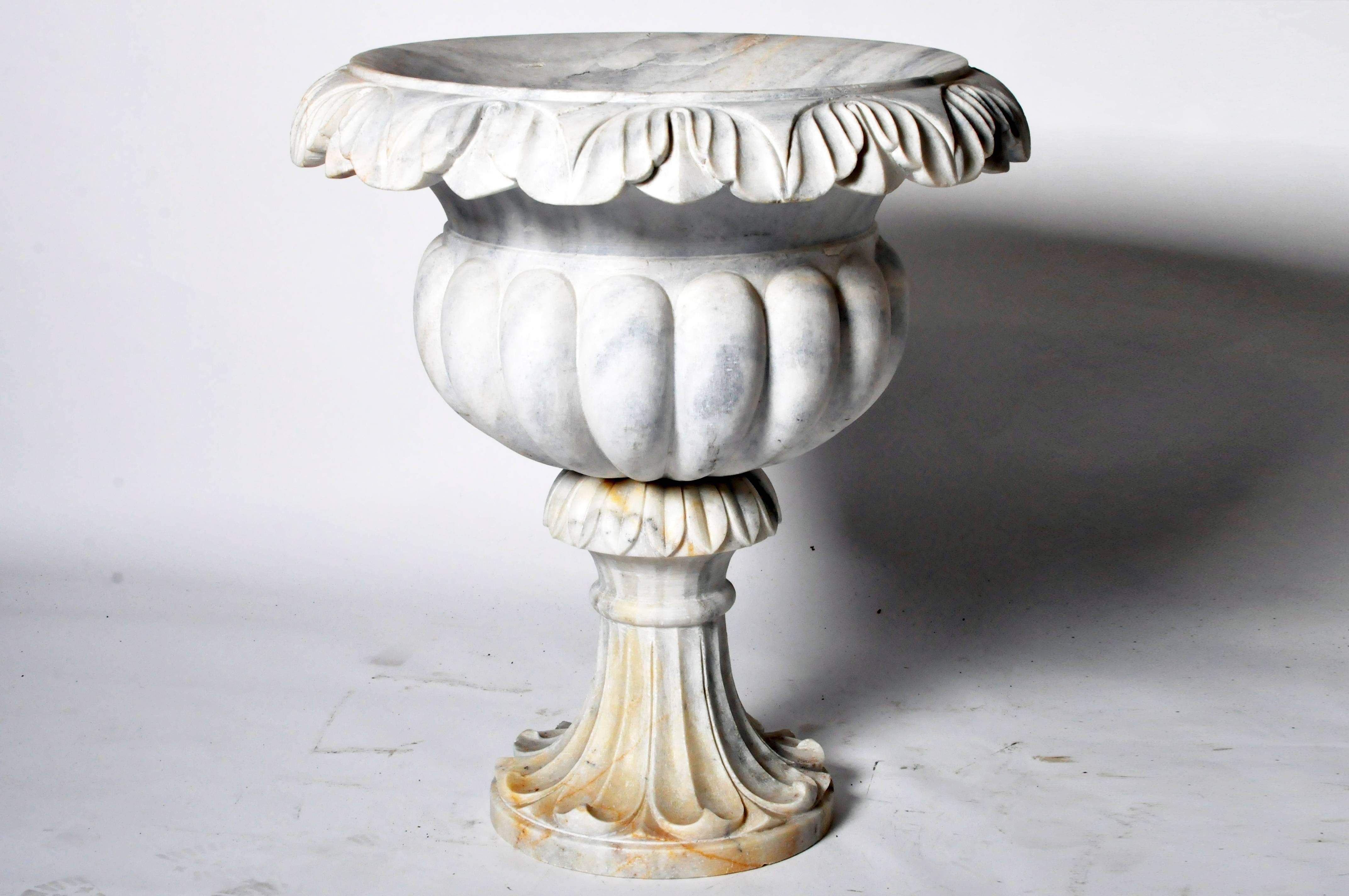 The variegated marble perfectly compliments these shapely urns. They are beautifully carved from the ruffled foliate rims, down through the ribbed bodies supported by frond patterned pedestal bases.
