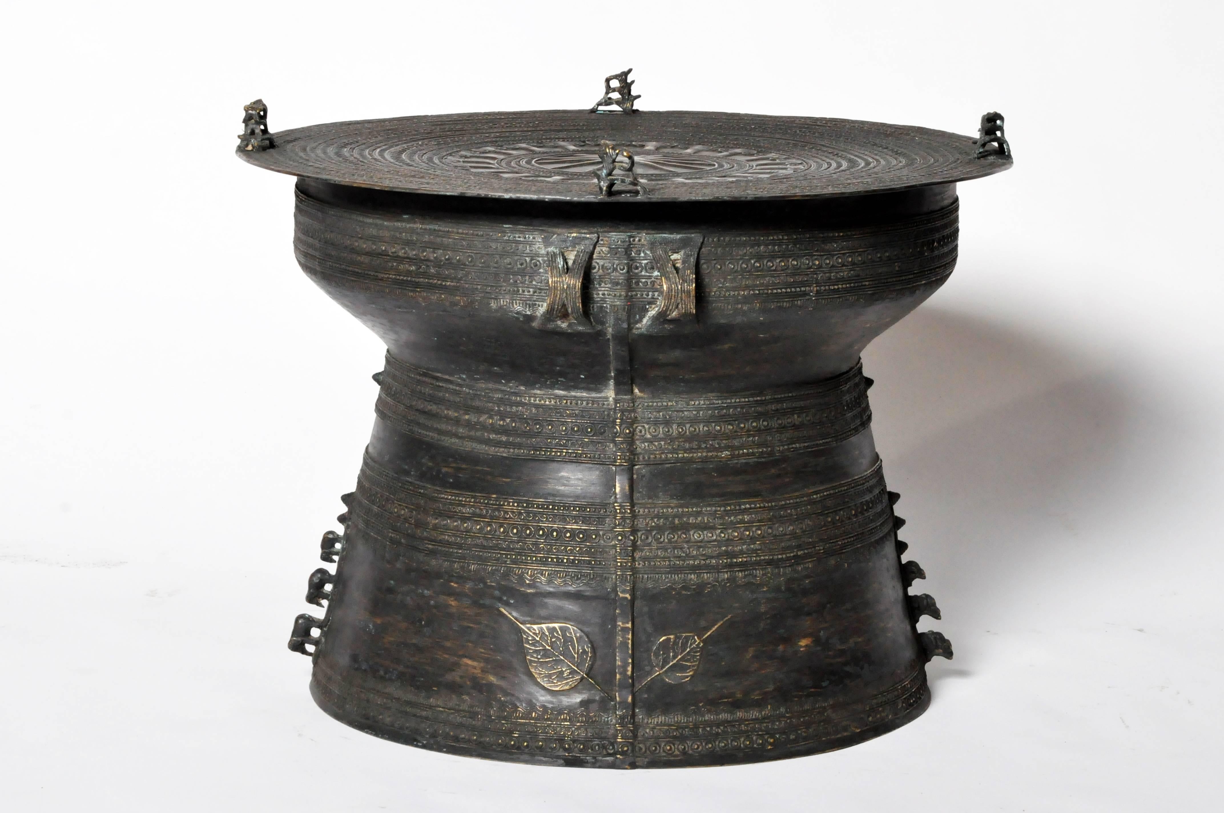 These handsomely patinated drums have circular tops with four double frog-form handles. Decorated with radiating bands and geometric patterns throughout, the waisted bodies are flanked by loop handles while their bases feature large leaf outlines
