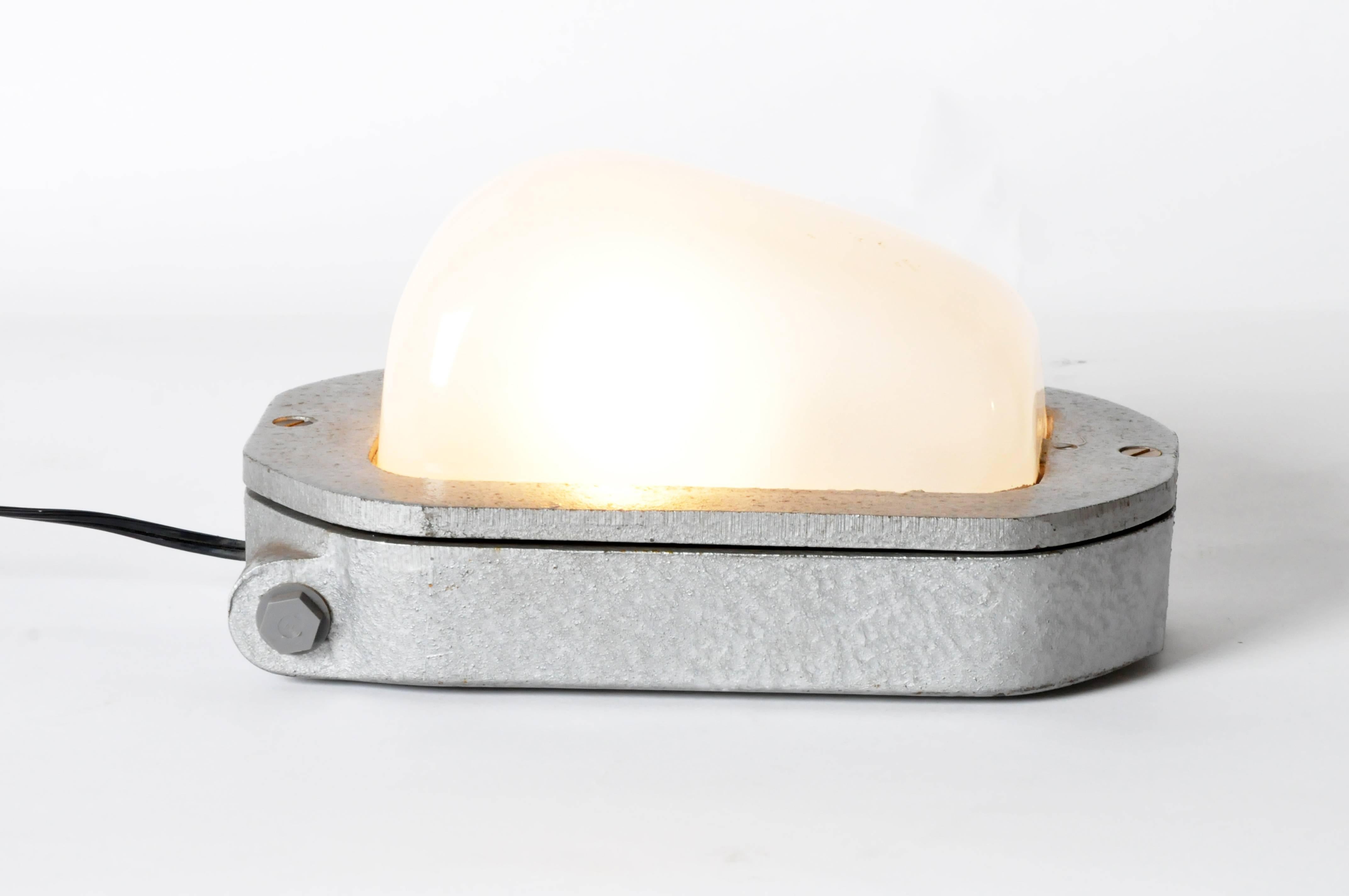 This fixture channels a nautical feel given its bulkhead lamp style. This light makes for an impressive sconce or tabletop lamp. The opaline-like glass dome is inset into the metal body, to which three felted feet have been added to protect the
