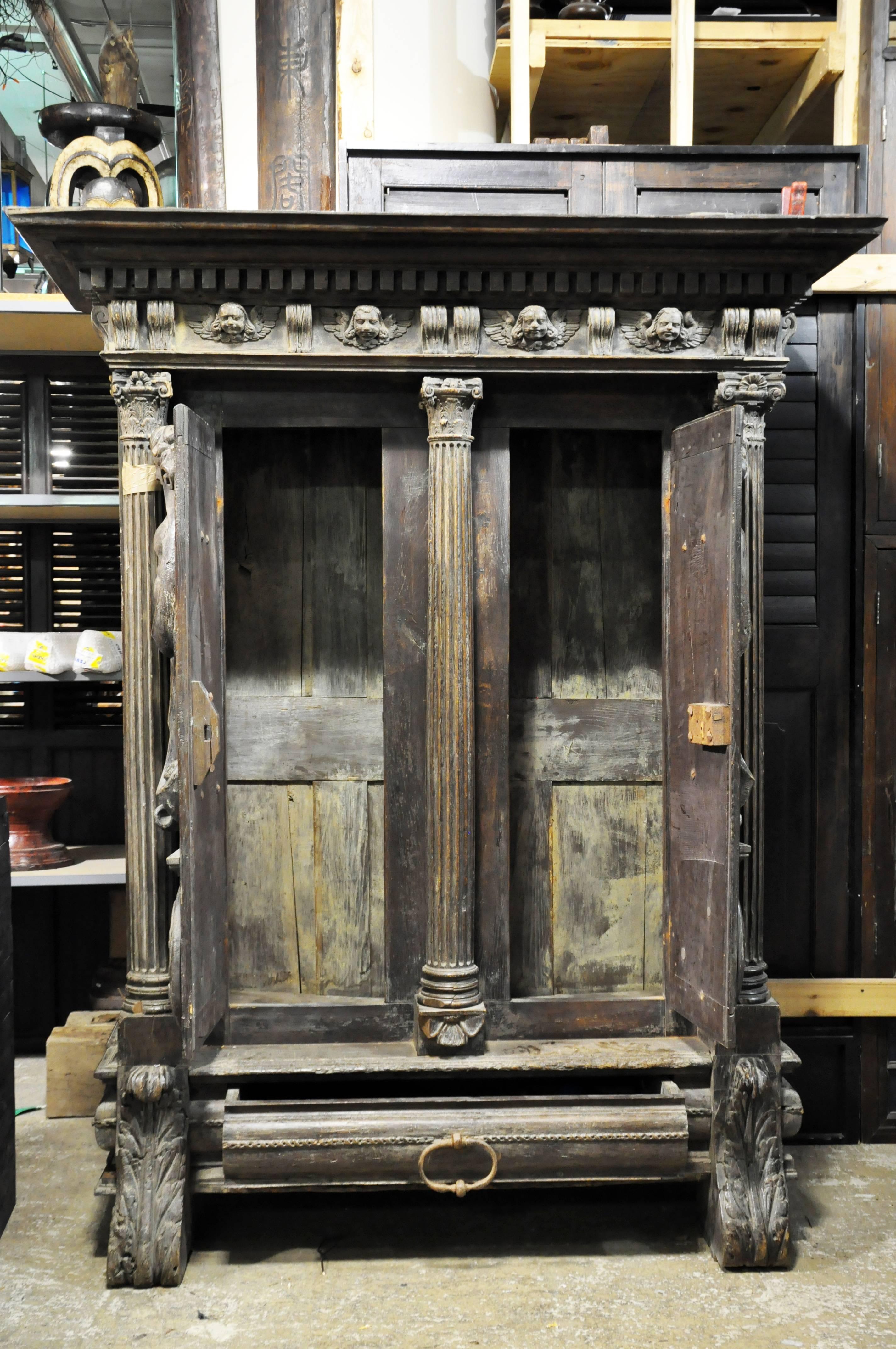 This handsome, well-patinated piece hails from Alsace, France. The molded and dentil cornice sits above a cherub-decorated frieze and stepped architrave that is supported by three Classic Corinthian order columns. Beneath ornate capitals and fluted