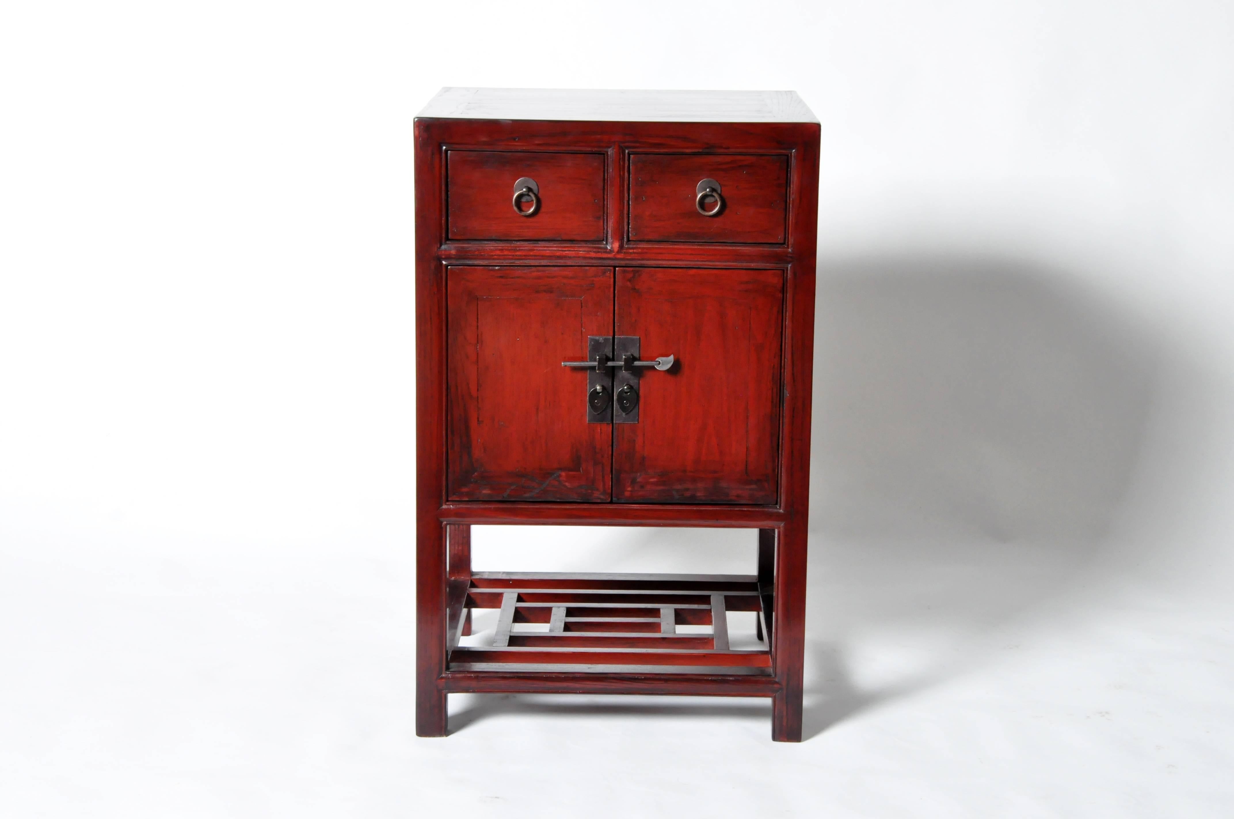 This Chinese side chest is made from red lacquered elmwood and has been fully restored. It features two drawers and a shelf for storage.
