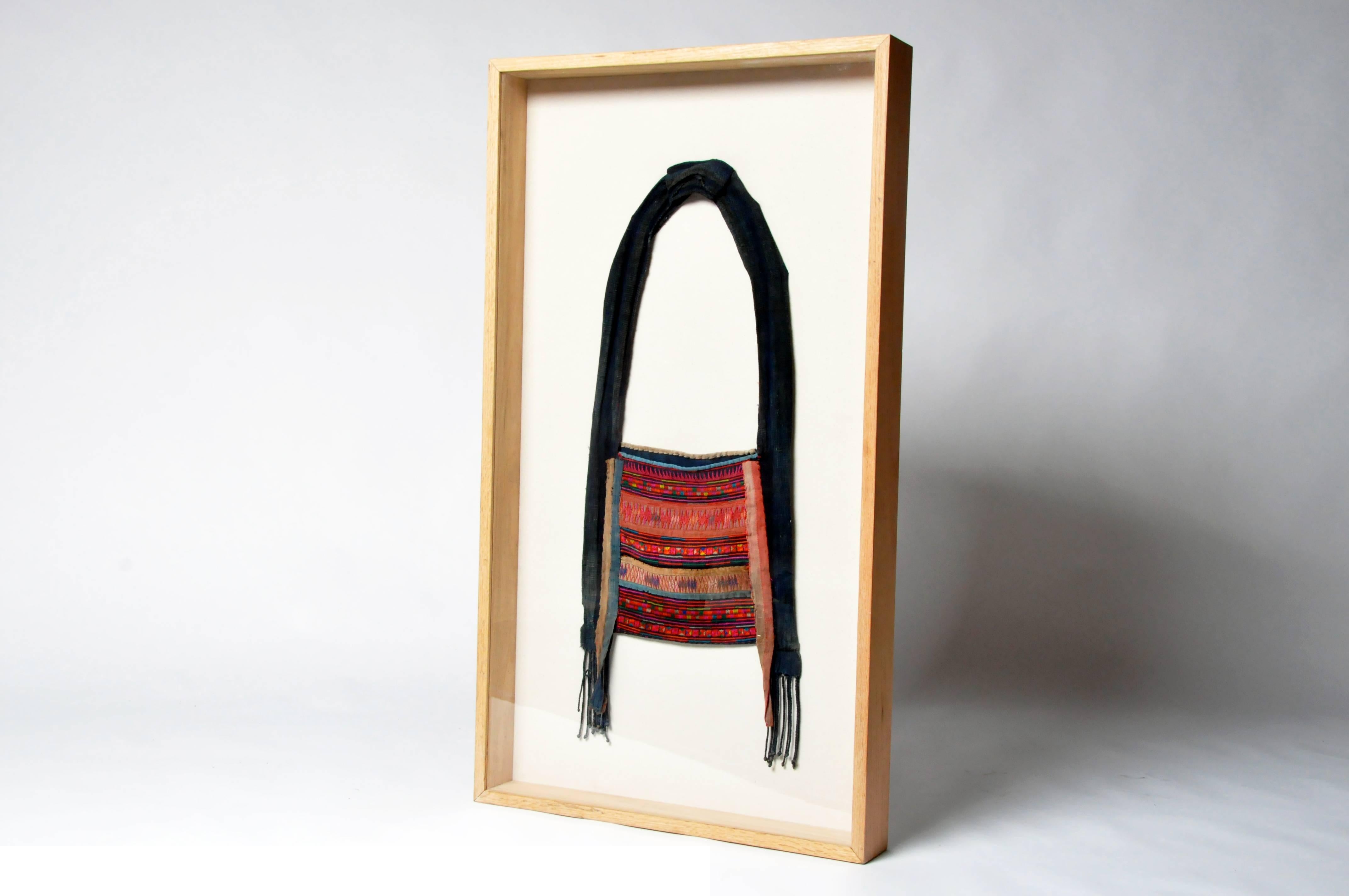 This hand embroidered shoulder bag is from the Akha tribe and has been framed for display on a wall. The Akha are an indigenous hill tribe who live in small villages at higher elevations in the mountains of Thailand, Burma, Laos, and Yunnan Province