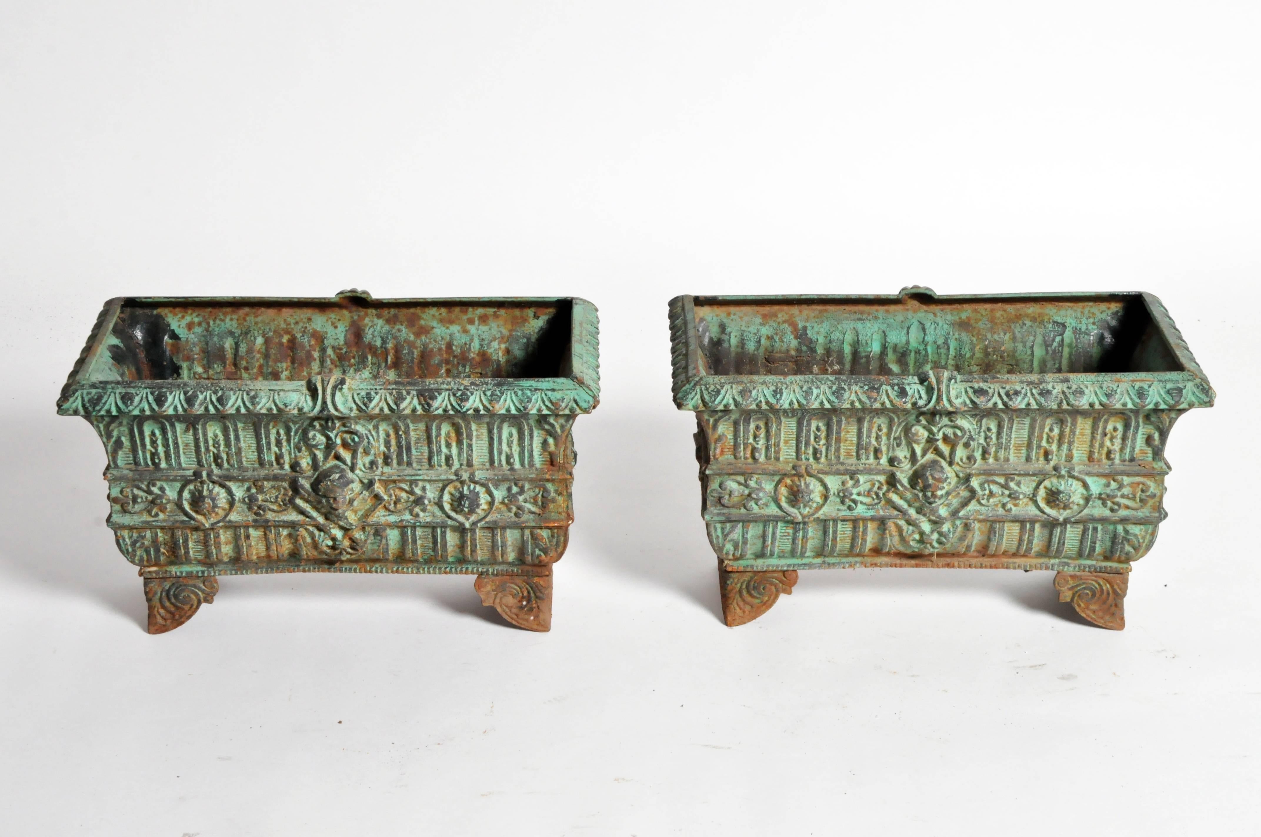 These stunning set of cast iron garden planters with Baroque motifs, putti, and scrolled feet. They are from France and the original blue-green patina is in excellent condition.
