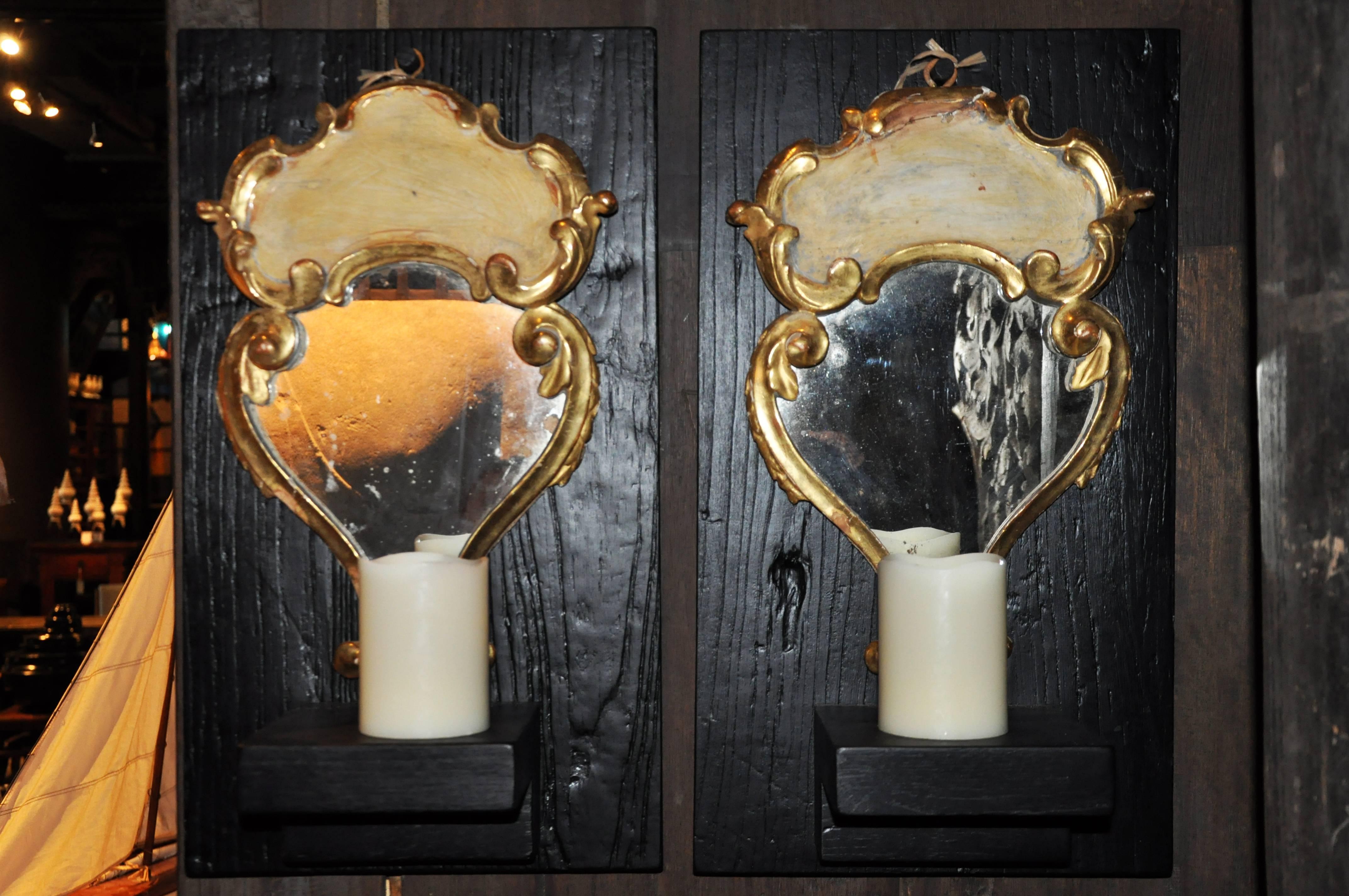 The acanthus leaf carved frames combine both S and C-scroll forms, which encircle the mirror plates as well as the shaped decorative panels that surmount them. The glass is original; however the delicate metal candle holders--which would have