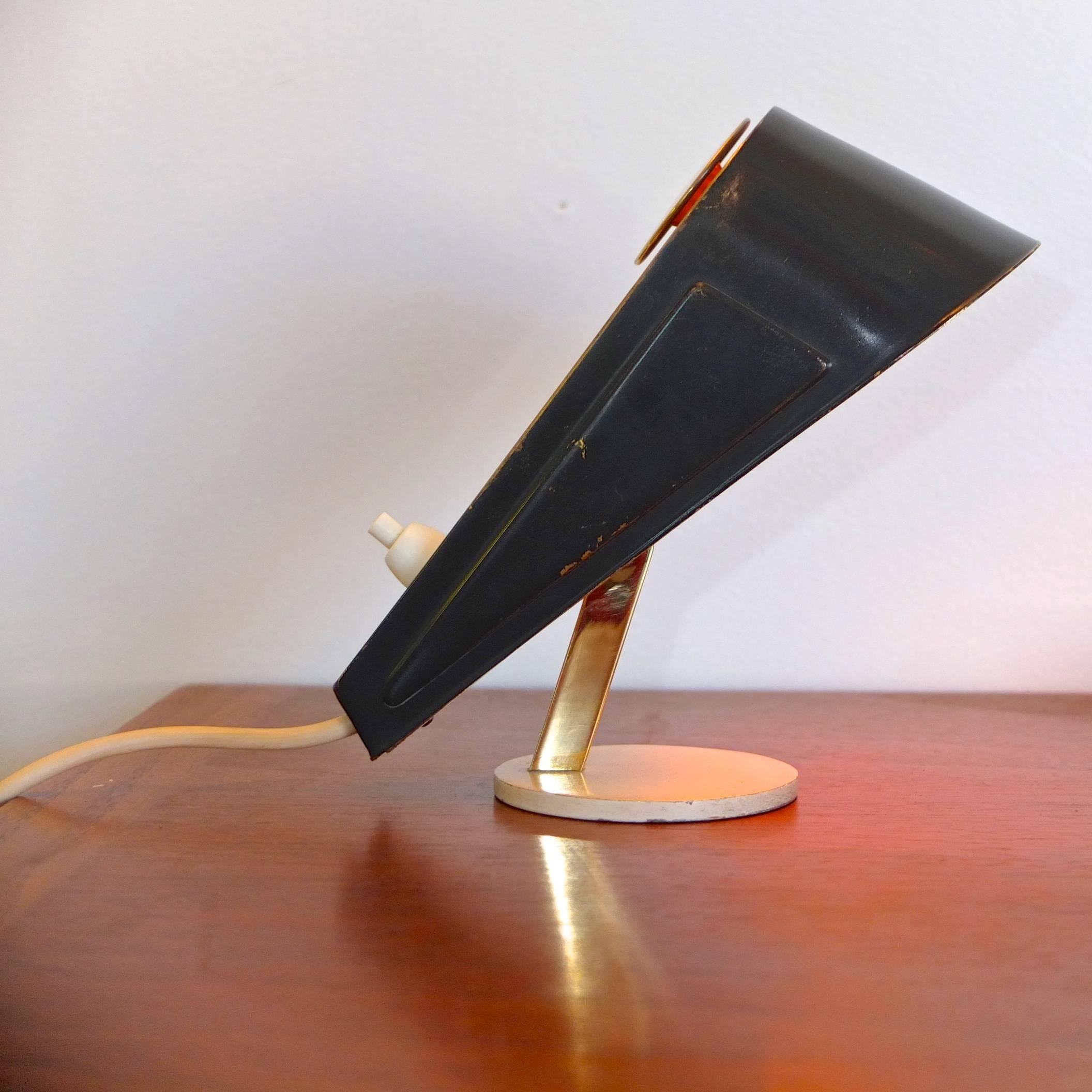 Articulating petite desk lamp in form of a wedge shaped door stopper. Enameled brass shade on brass stem on round enameled metal disk base. Takes one E14 candelabra bulb. Heavy white cord with two pronged European plug (adapter provided). Push