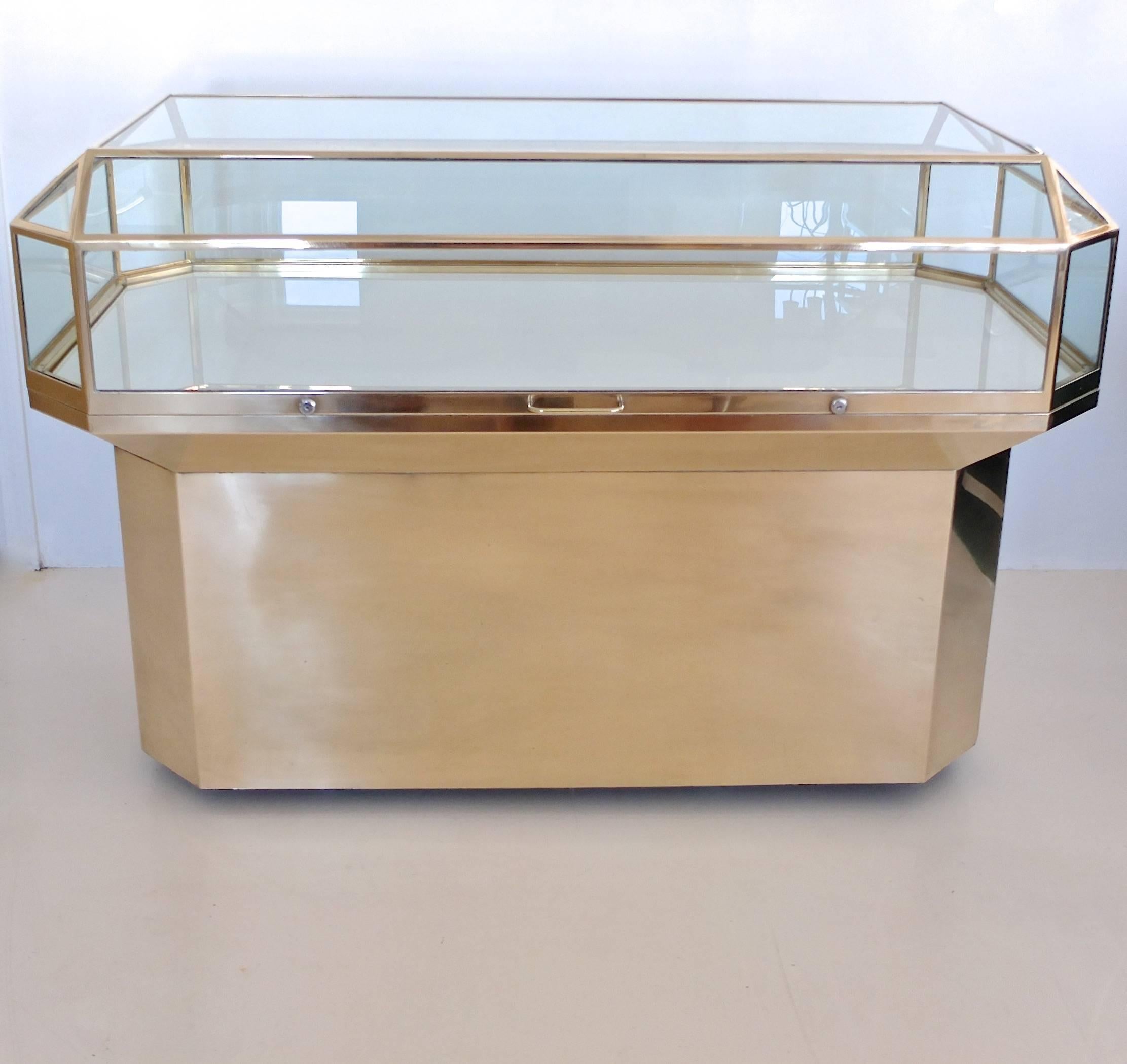 Matched pair of custom display cases in solid brass and glass with faceted emerald cut brass framed glass top attached to a recessed brass clad hexagonal pedestal base, finished in the round for 360 degree viewing. The top has two locks on either