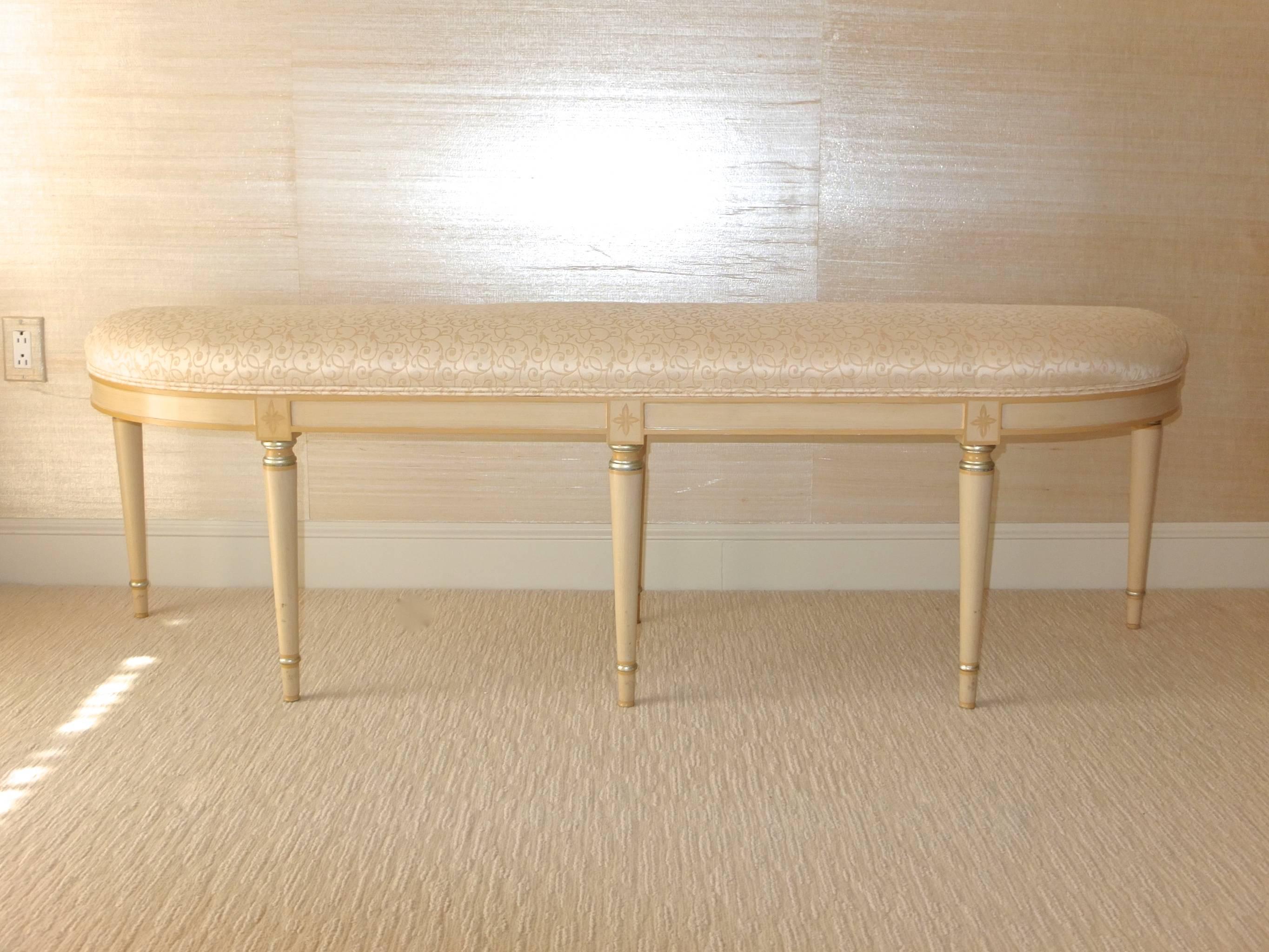 Demilune upholstered bench, neoclassical form with six turned tapered wood legs, ivory lacquered with platinum leaf embellishments and cream trim. Original Brunschwig and Fils silk matelassé silvery white upholstery in excellent condition.