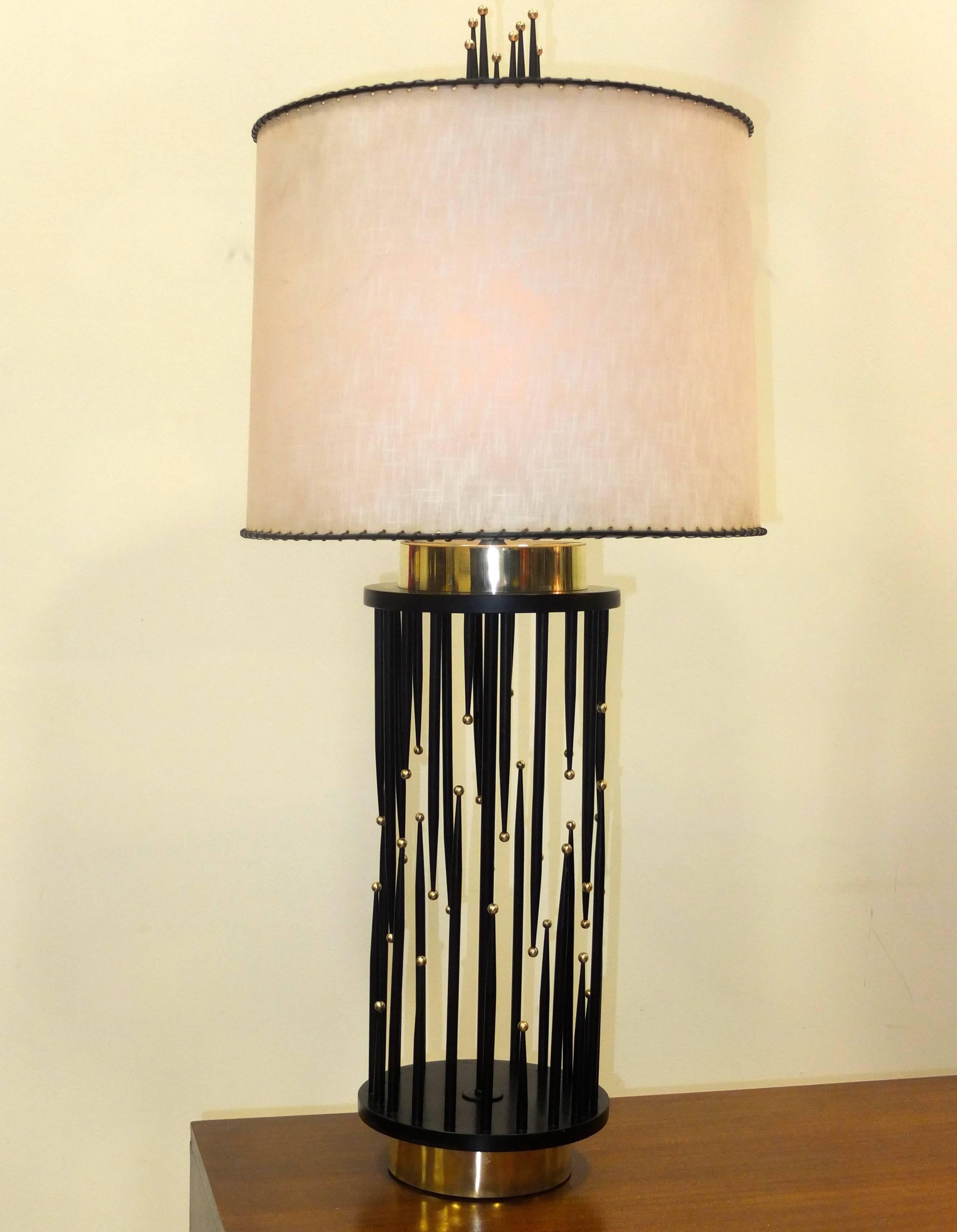 Lámpara de sobremesa vintage de los años 60, visualmente llamativa, con una base cilíndrica compuesta por puntas cónicas negras que son espigas de madera pintadas a alturas irregulares y cada una con una bola de latón macizo en la punta.  Base y