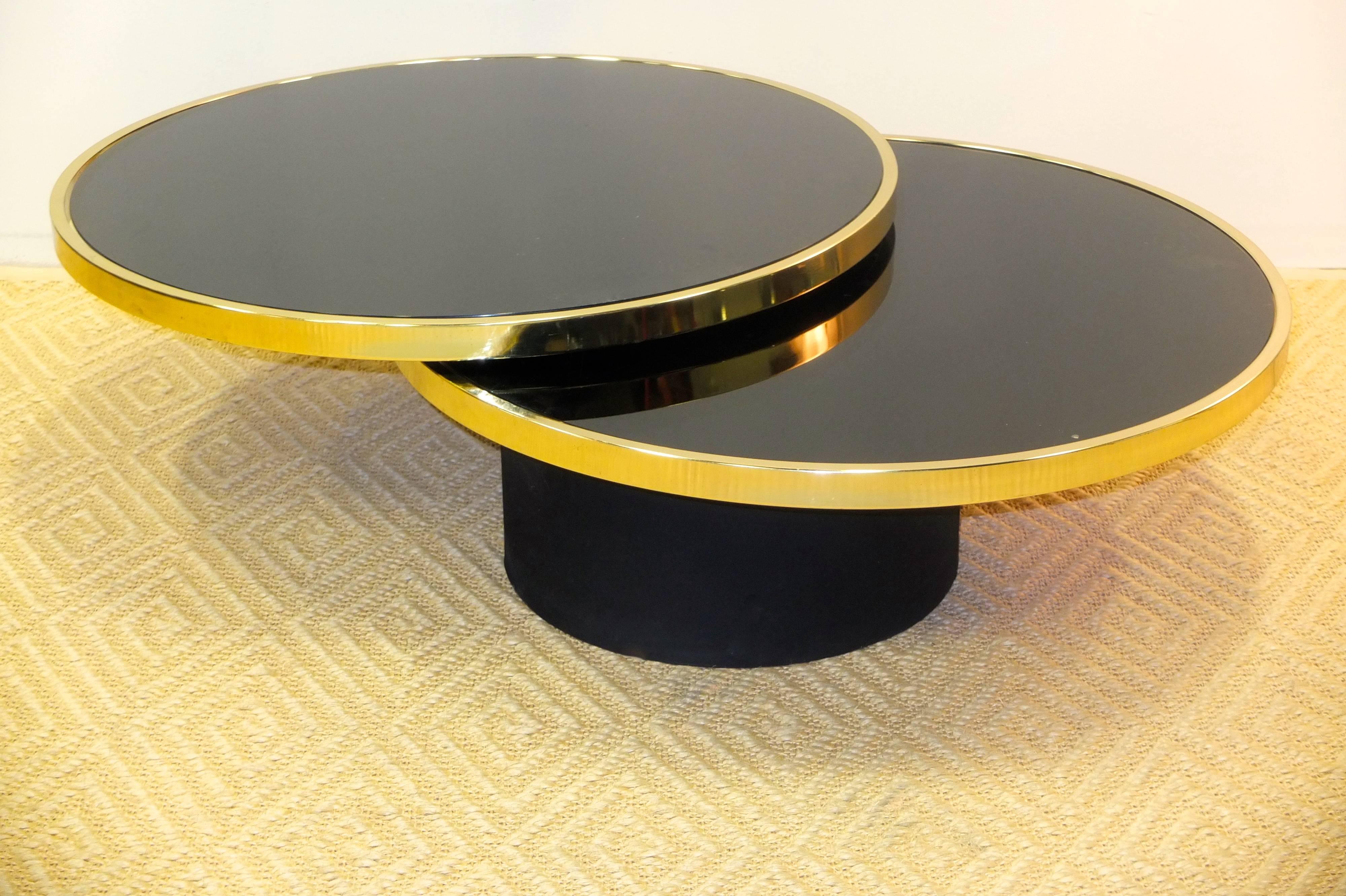 Glamorous and functional round two tier cocktail table the top tier of which rotates smoothly on a clever swivel mechanism.  The base is a drum covered in black suede.  The brass plated double ring frames hold round glass tops which have been tinted