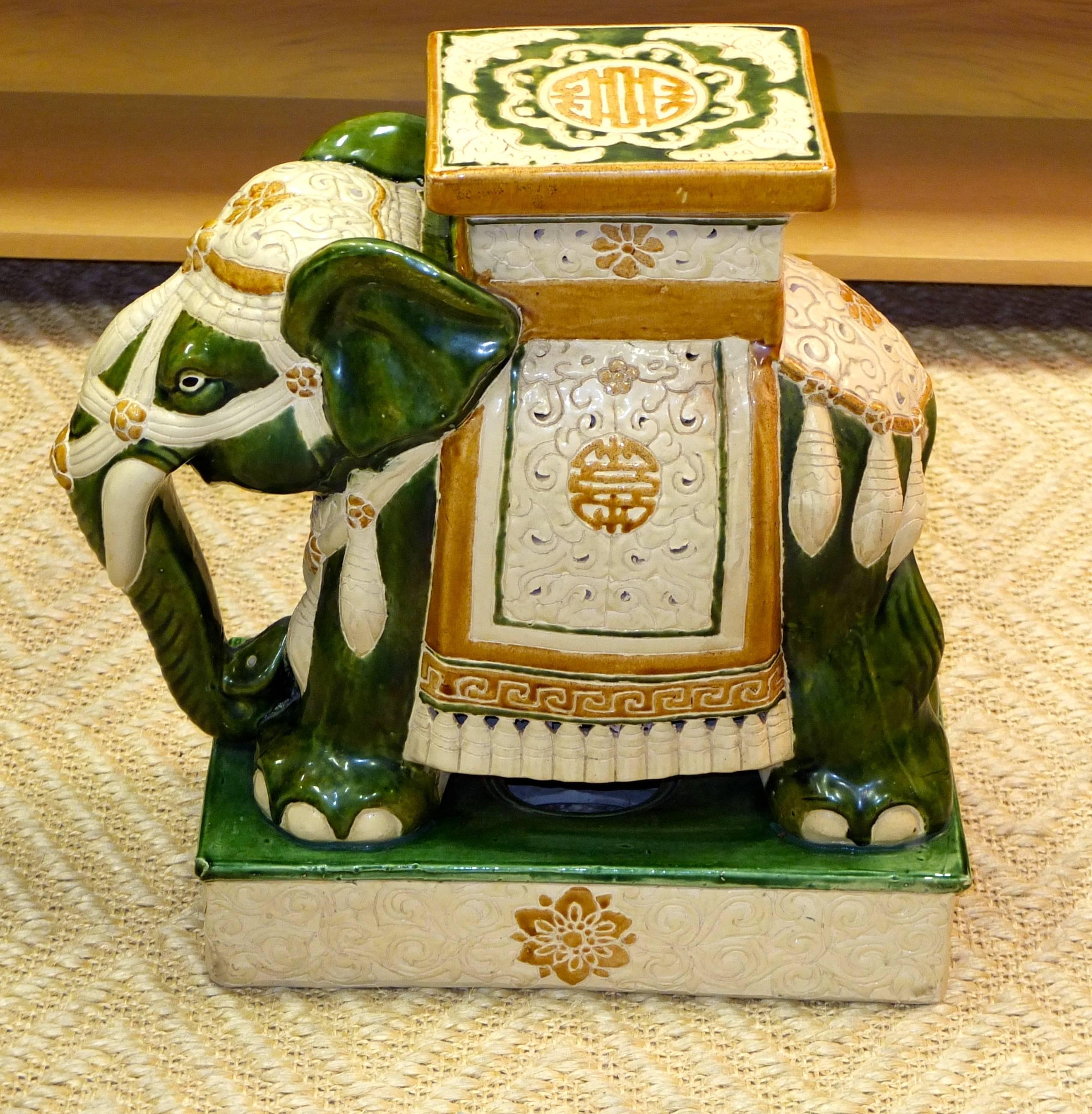 Mid-20th century glazed green ceramic elephant garden stool bedecked with ivory and golden amber glazed saddle and decorations.

There appears to be a signature on the elephant's left rear foot.

Can also be used as a side table with a glass top.