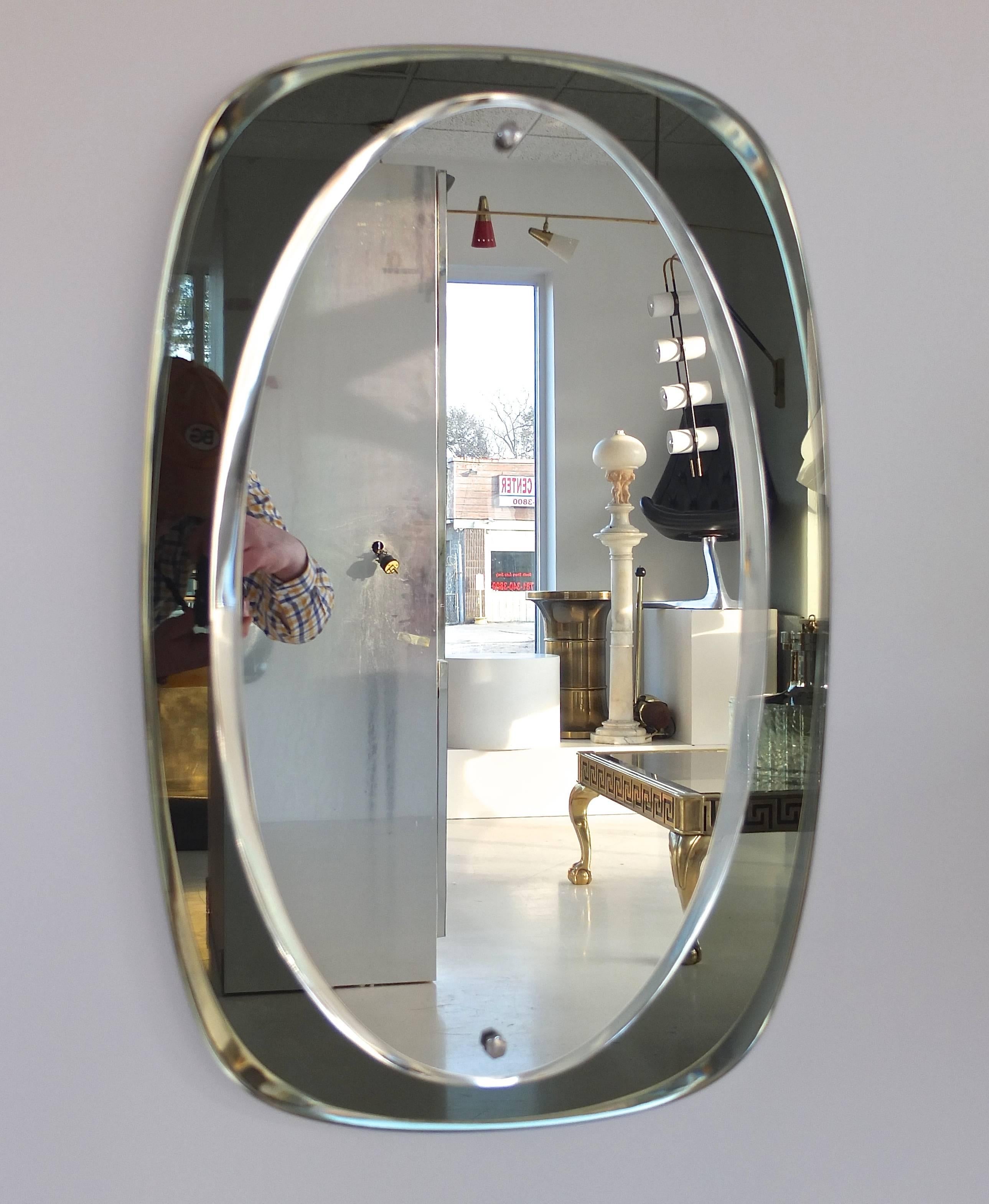Mid-Century Modern Italian wall mirror by crystal Art, circa 1955. Oval shaped beveled mirror with a dark smokey green color glass cushion form outer frame, bonded with two chrome plated hexagonal fittings.

   