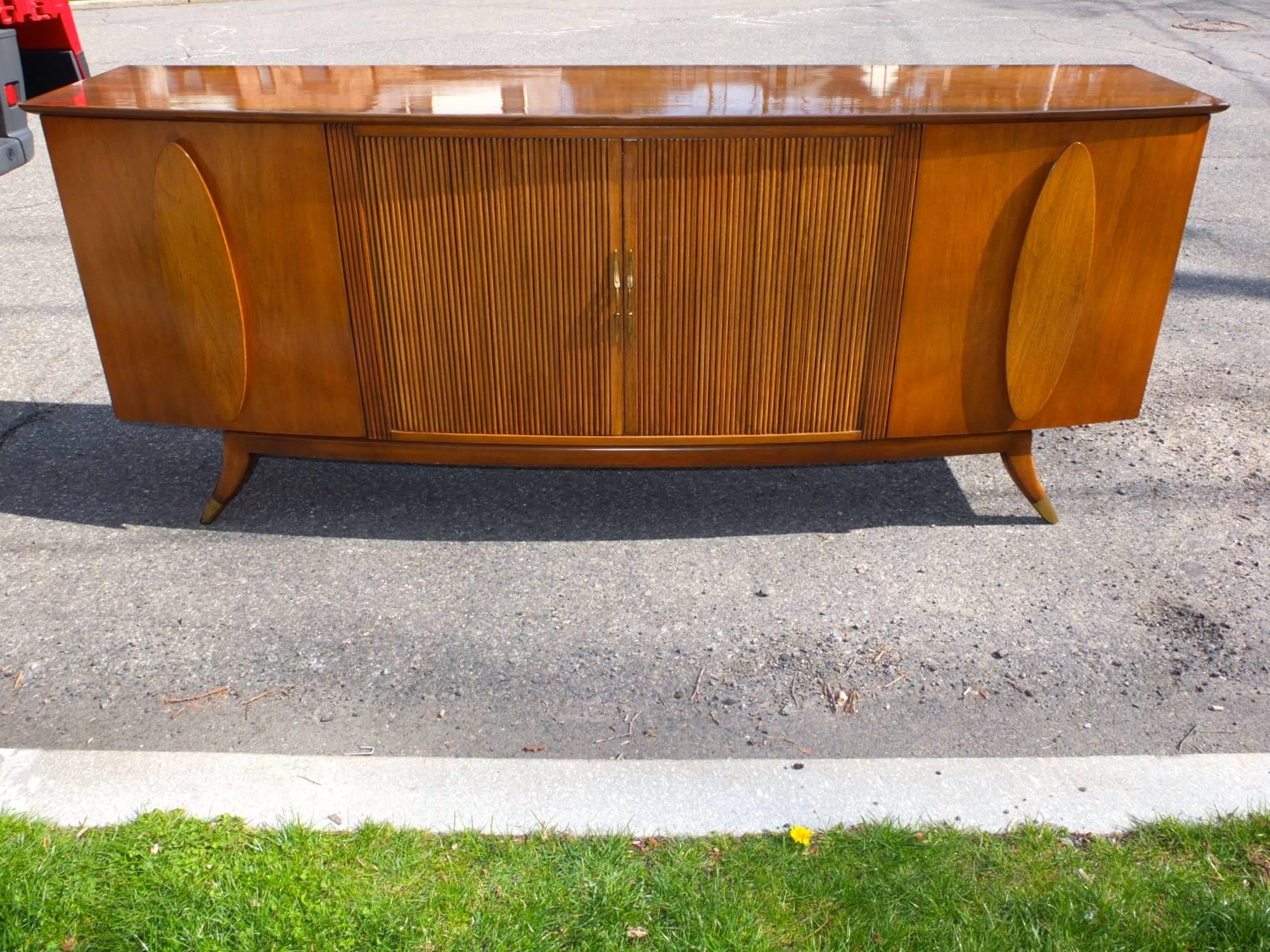 SATURDAY SALE

Long bow-fronted credenza sideboard in walnut with two cabinet doors and four drawers behind sliding tambour doors with brass pulls. The top two drawers are lined and divided for silverware. The two side cabinets each have two