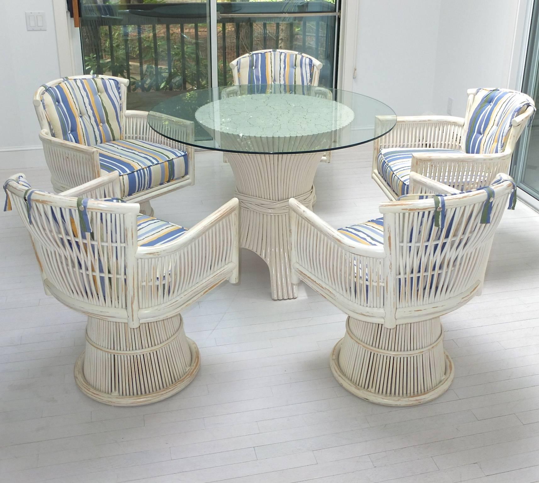 California modern sun room dining set with table and five armchairs. 
Off-white lacquered bamboo sheaf pedestal base dining table raised on arched supports with a 42 inch round beveled glass top.
Five rattan wicker swivel armchairs with round