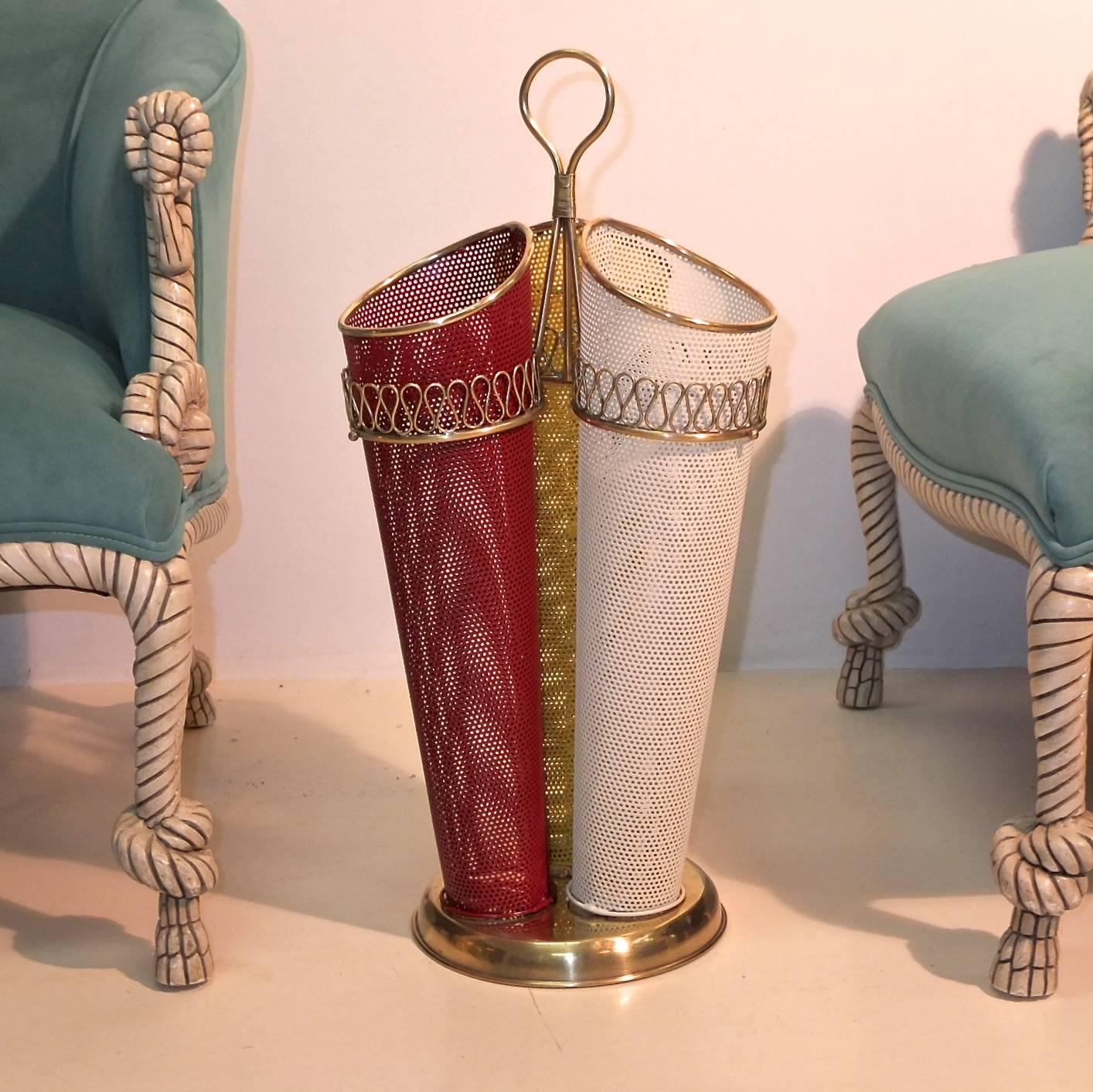 Italian 1950s umbrella holder with brass serpentine embellishments as seen on the mirrors of Gio Ponti. Three perforated metal cones trimmed in brass, lacquered ivory, yellow and red on a round brass base with a brass looped ring finial. 

A