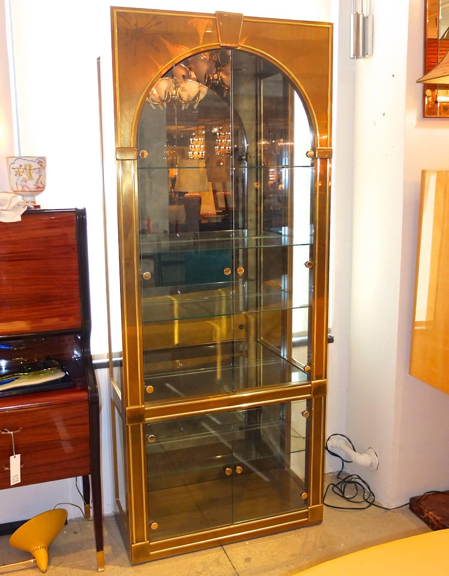 Mastercraft model 326 vintage 1970s Palladian style brass, glass and antiqued smoked mirror vitrine display curio cabinet, designed circa 1970 by William Doezema.  
Measures: 84 in. H x 34 in. W x 15.5 in. D. 
Four clear glass removable shelves and