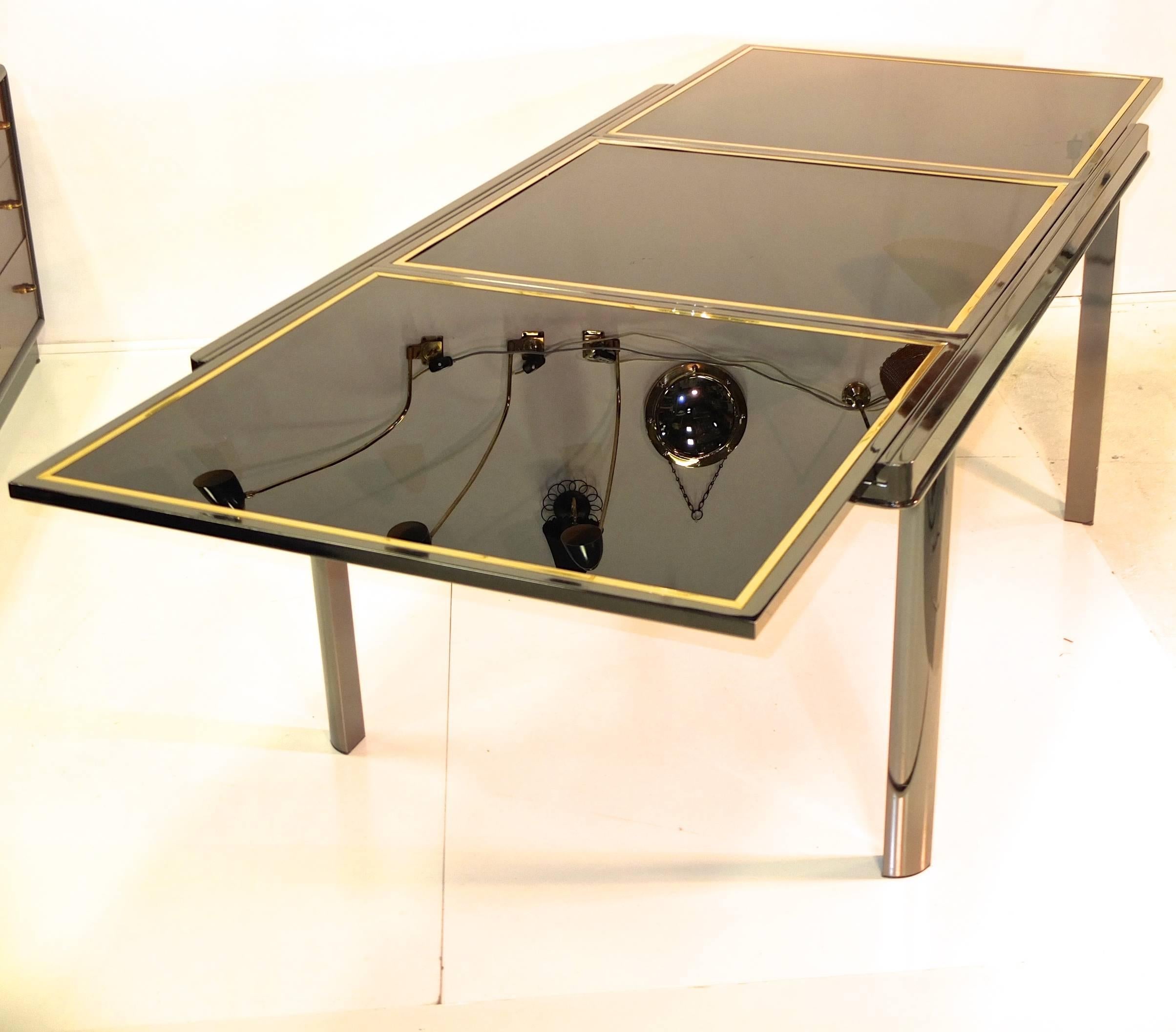 Vintage dining table in the style of Milo Baughman constructed of smoked chrome-plated steel with extendable top of three black glass panes trimmed in brass. Two panes easily slide horizontally revealing a hidden middle pane which pivots into place.