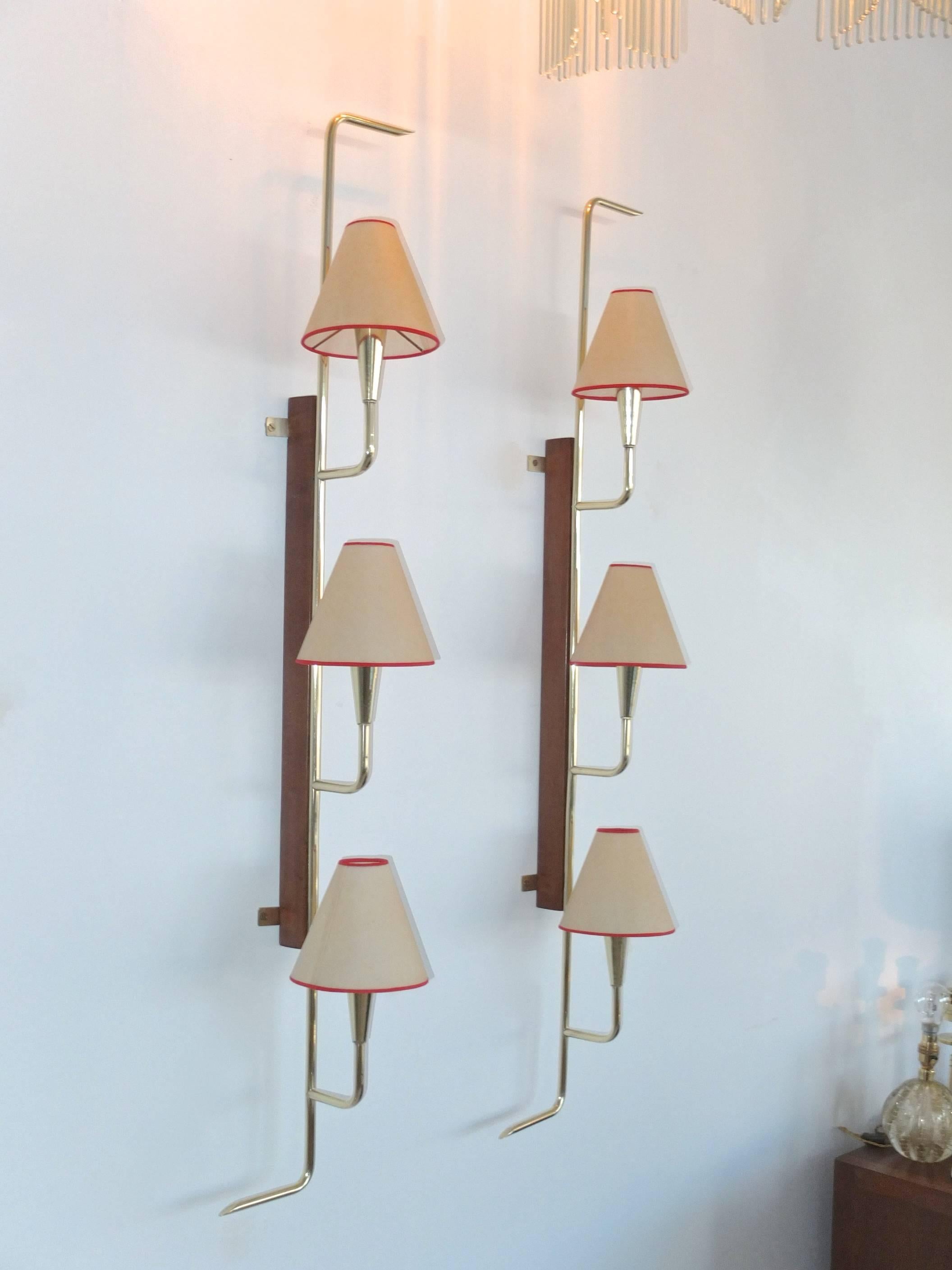 Quality pair of bracket sconces produced in France in the 1950s each with three brass cone socket lights extending from a vertical brass tube finished on top and bottom with right and left pointing finial detail, supported by a solid walnut
