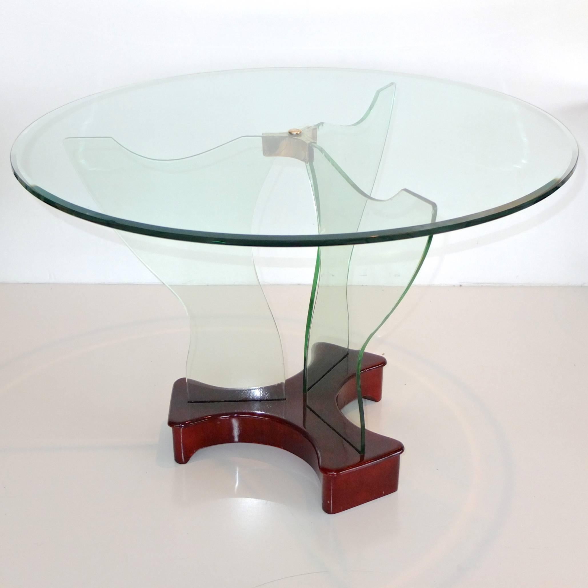 Italian Art Deco 1930s cocktail table by Luigi Brusotti, Milano with round bevelled glass top fastened by brass mount to three panels of shaped securit glass supports mounted on lacquered mahogany clover form base. 

Measures: 21