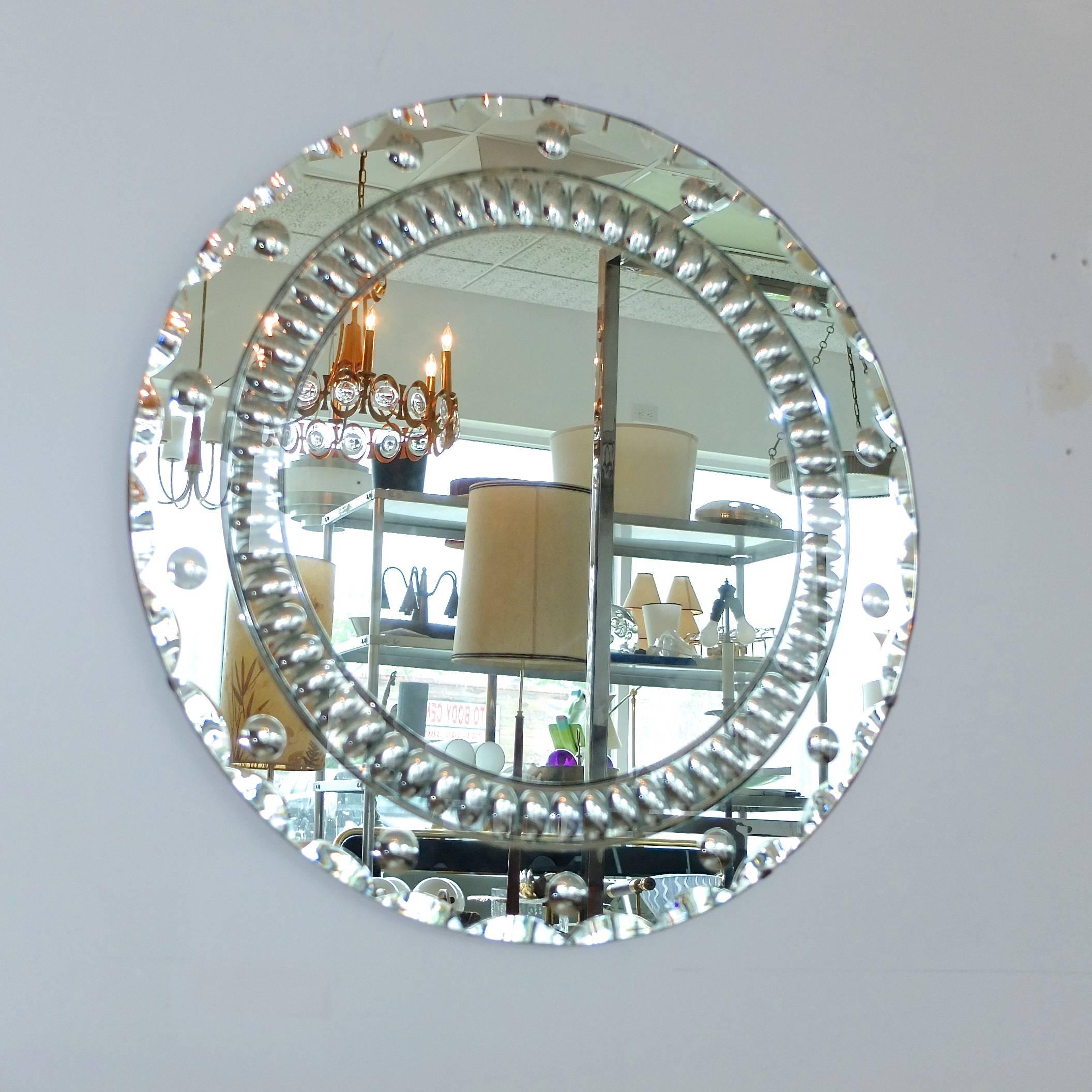 1940s silvered round mirror with an abundance of ground optical motifs including ribbon scalloped edge, 14 convex/concave optic bubble bullseyes and a stunning egg and dart motif inner garland.

Mirrored glass is clipped to wood backing. Hangs via