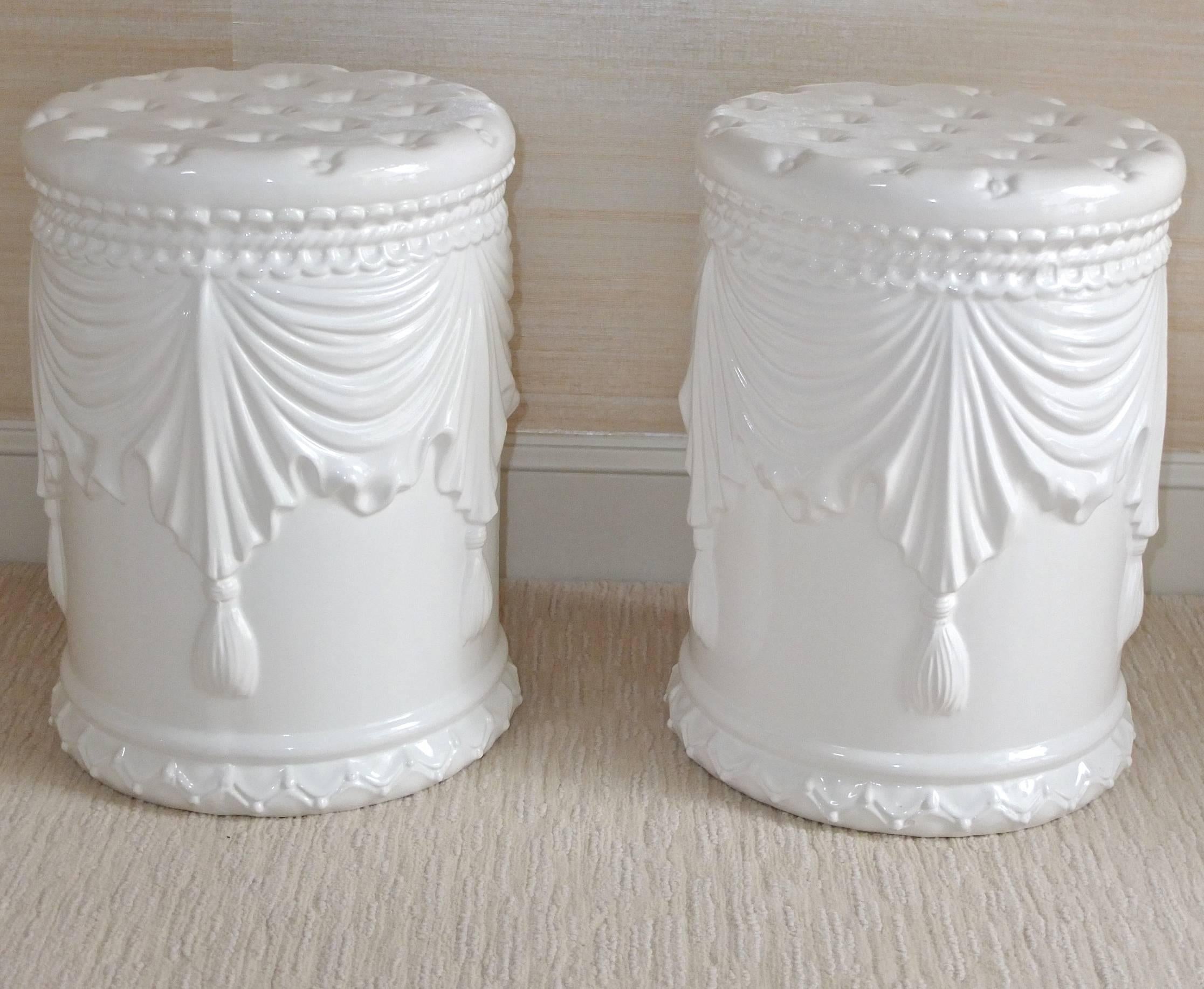 Pair of white ceramic garden stools molded with tasselled drapes and quilted cushion seat. Excellent condition.