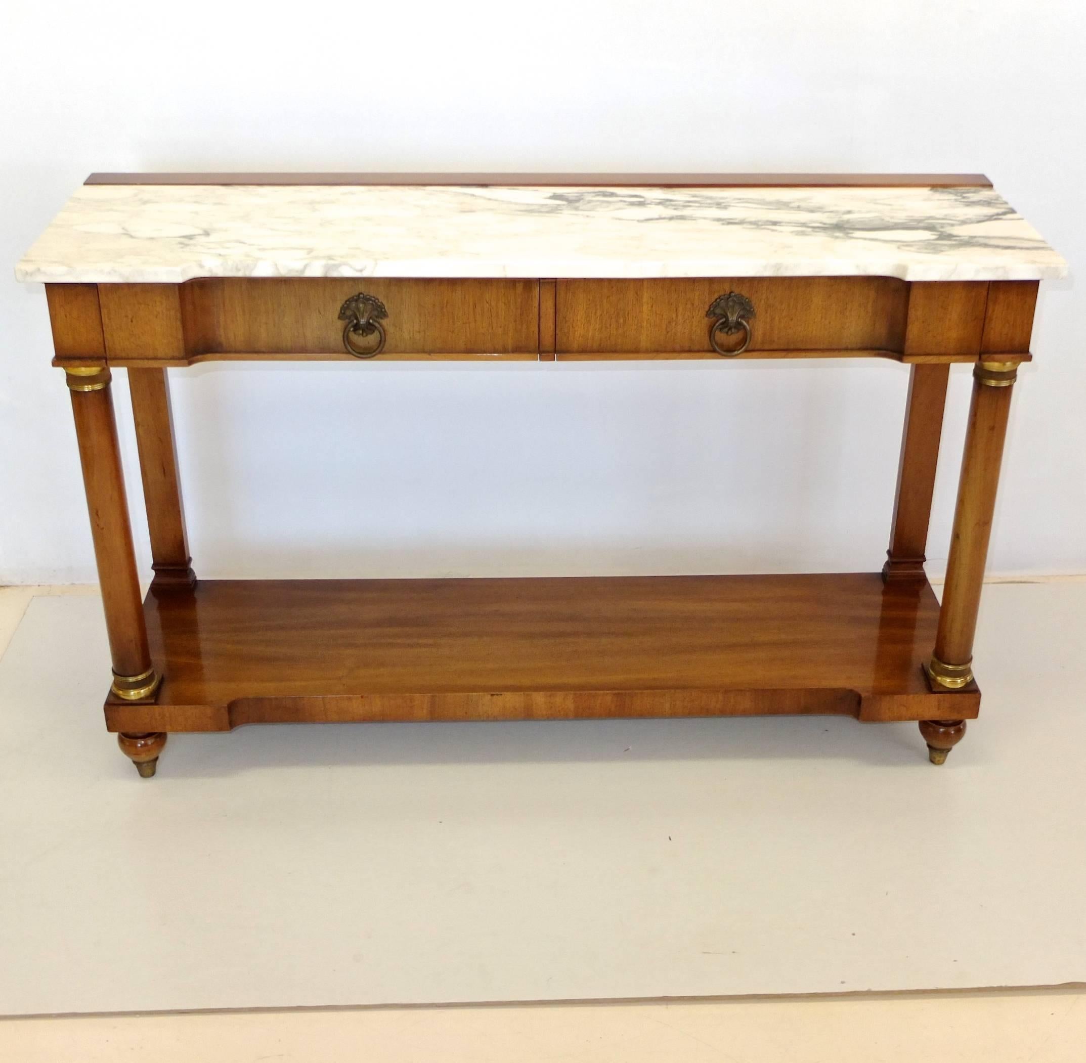 Empire style console table by John Widdicomb, circa 1960. Notched front edge white with black/gray marble top over two drawers having dovetail construction and brass ring pulls, supported by two turned columns with ormolu mounts and two flat colums