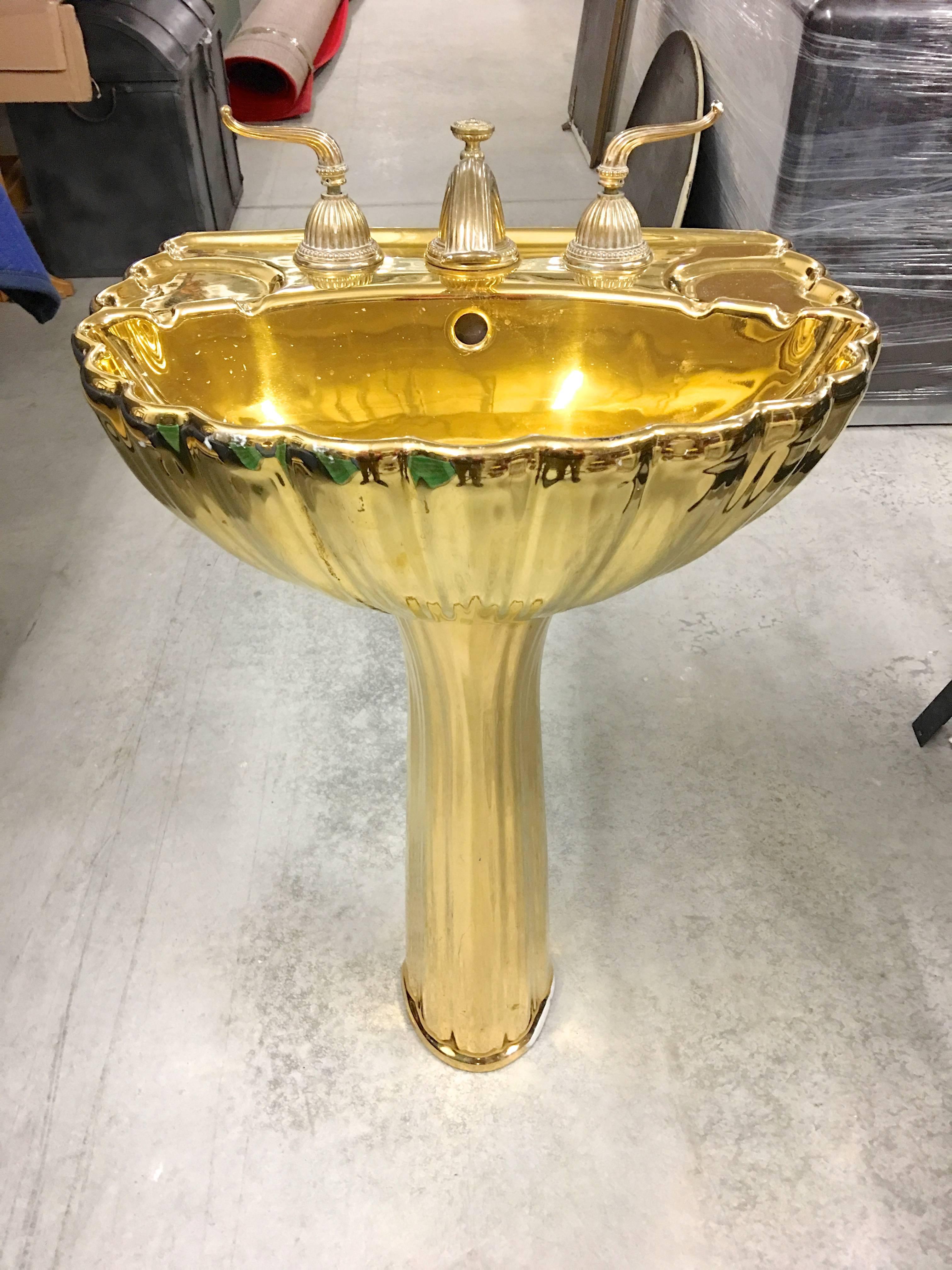 Golden mirror polished brass colored porcelain pedestal sink, attributed to Sherle Wagner. Shell form basin. 
Original gold finished waterworks. Dimensions - 36 inches high by 20 inches wide by 16 inches deep.
