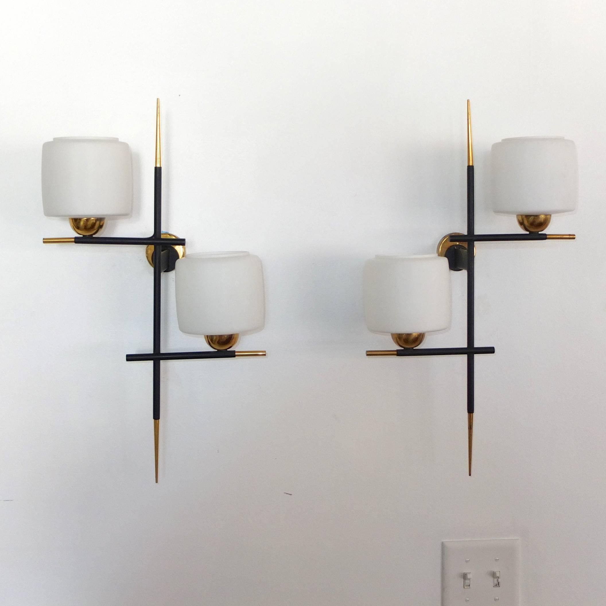 Pair of modernist linear sconces comprised of matte black enameled brass tubular criss crossing structure with solid brass spiked finials and opaline glass open globe shades.

Designed by Gaston Fossati for Ateliers d'Art d'Uzes.

Often mistaken