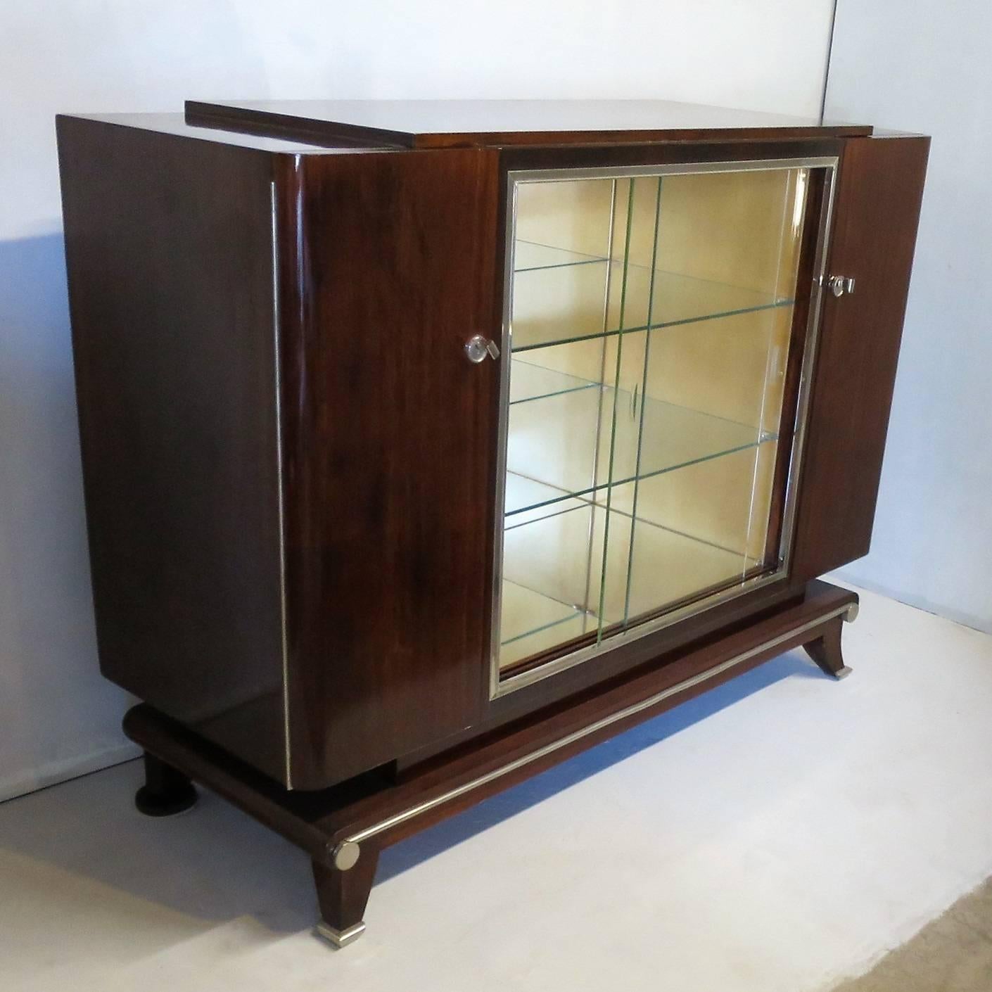 Display cabinet-bar, French Art Deco period, in mahogany, mirrors inside the piece.
The piece is standing on a very elegant design base with curved legs.
Glass shelves inside the middle part, shelves inside both side parts.
This piece more than